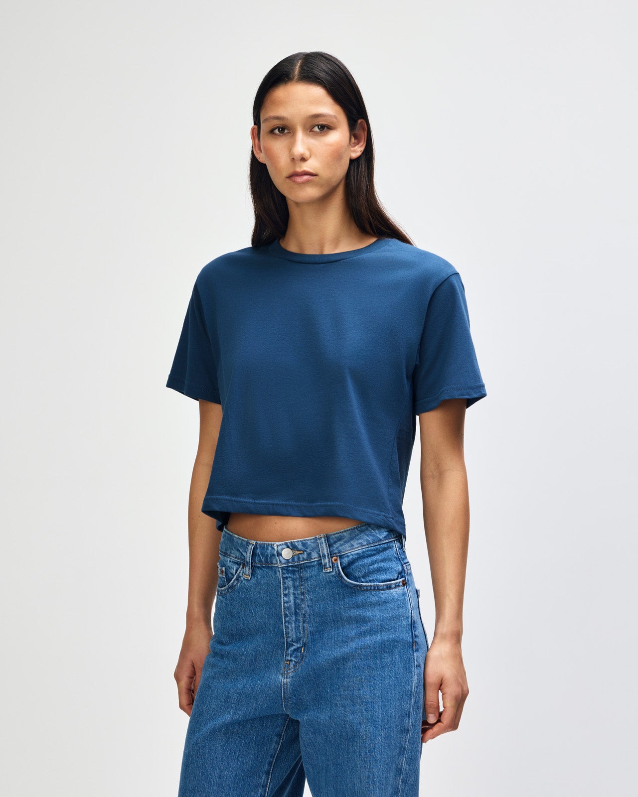 Female model wearing an American Apparel Fine Jersey Women's Boxy Tee in Sea Blue, paired with blue jeans, standing against a plain background (front pose) -sea blue