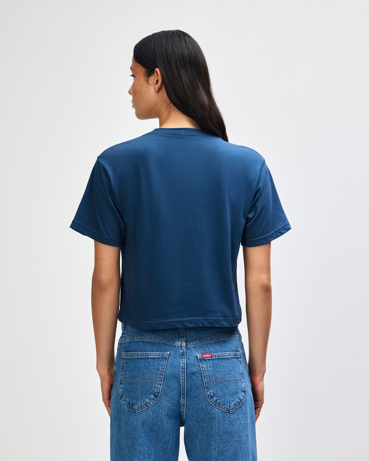 Female model wearing an American Apparel Fine Jersey Women's Boxy Tee in Sea Blue, paired with blue jeans, standing against a plain background (front pose) -sea blue