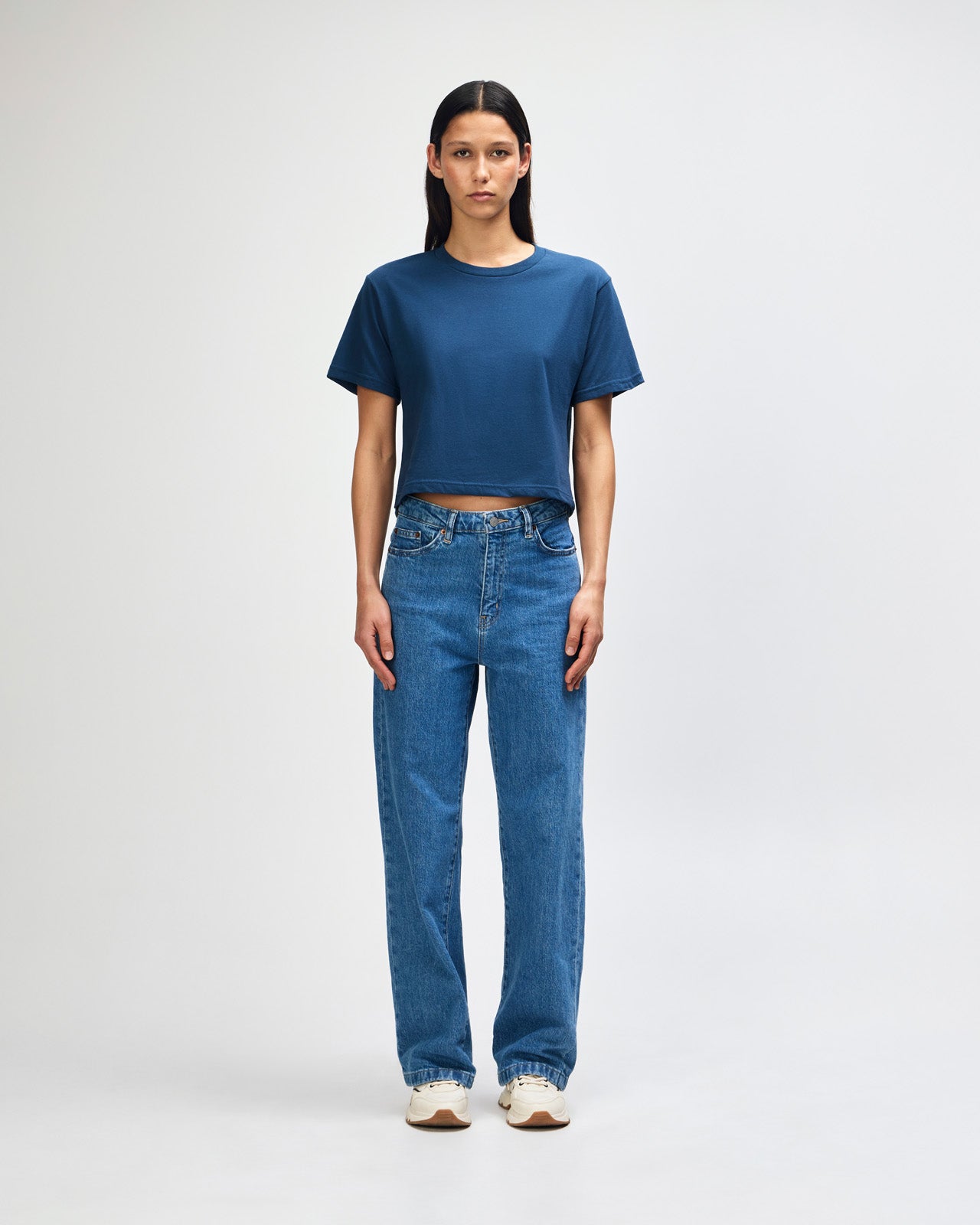 Female model wearing an American Apparel Fine Jersey Women's Boxy Tee in Sea Blue, paired with blue jeans, standing against a plain background (front pose) -sea blue