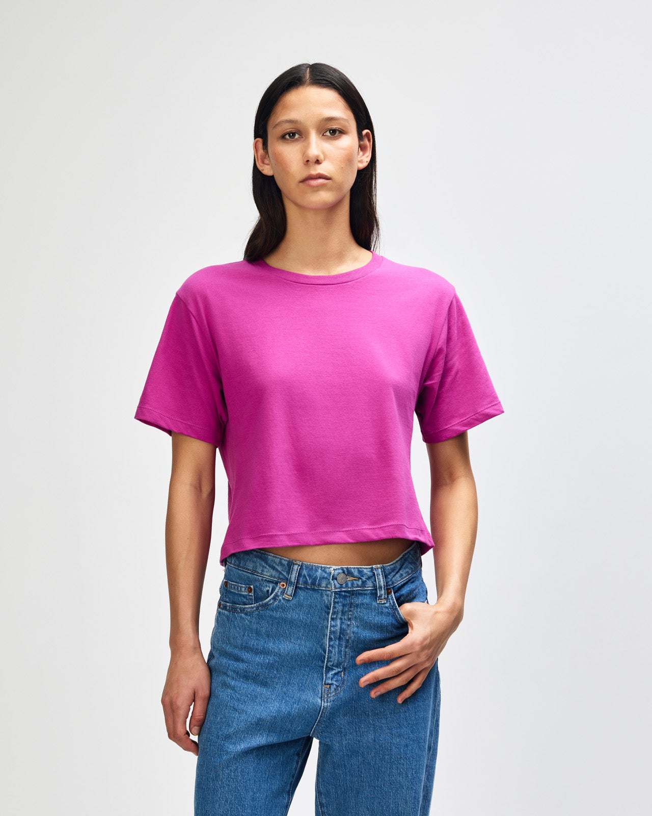 Female model wearing an American Apparel Fine Jersey Women's Boxy Tee in Super Pink, paired with blue jeans, standing against a plain background (front pose) -super pink