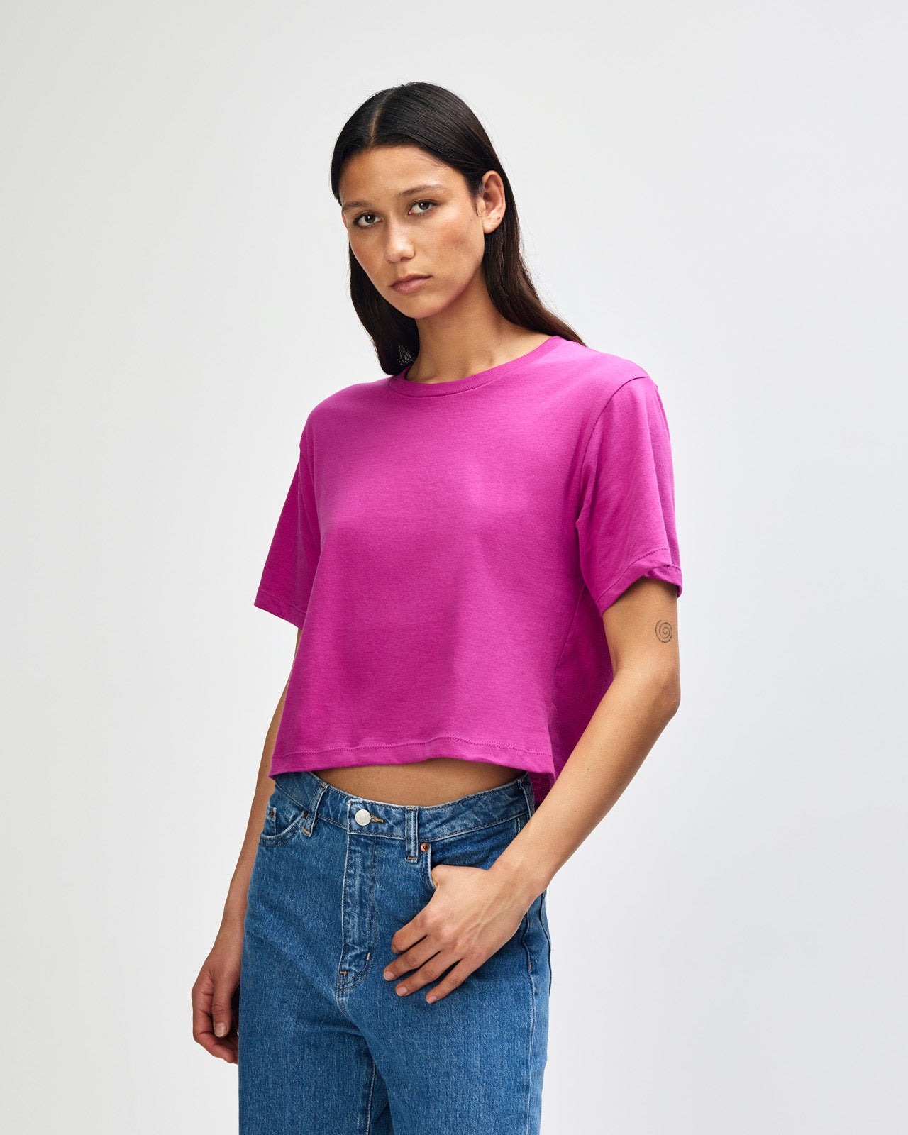 Female model wearing an American Apparel Fine Jersey Women's Boxy Tee in Super Pink, paired with blue jeans, standing against a plain background (front pose) -super pink