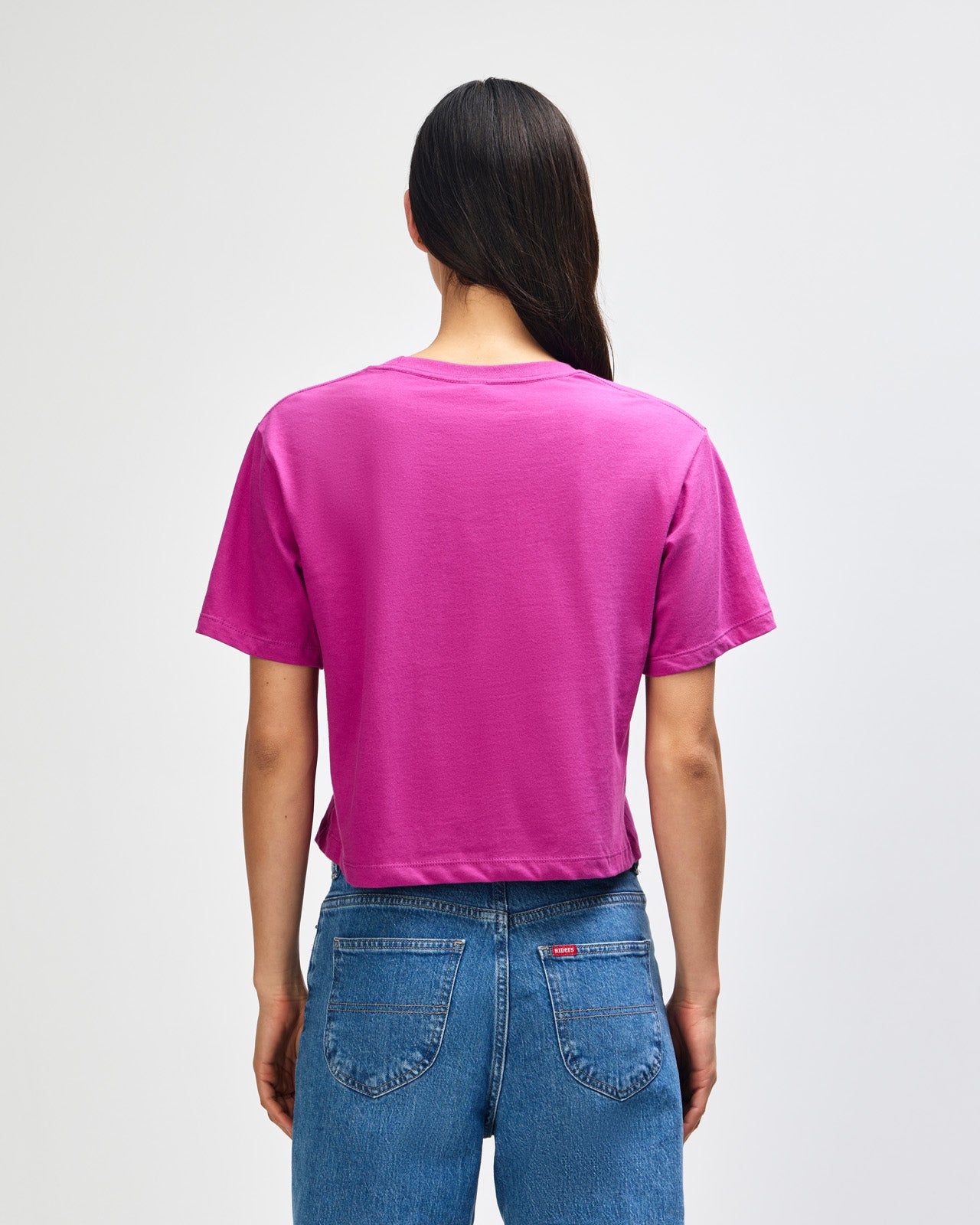 Female model wearing an American Apparel Fine Jersey Women's Boxy Tee in Super Pink, paired with blue jeans, standing against a plain background (front pose) -super pink