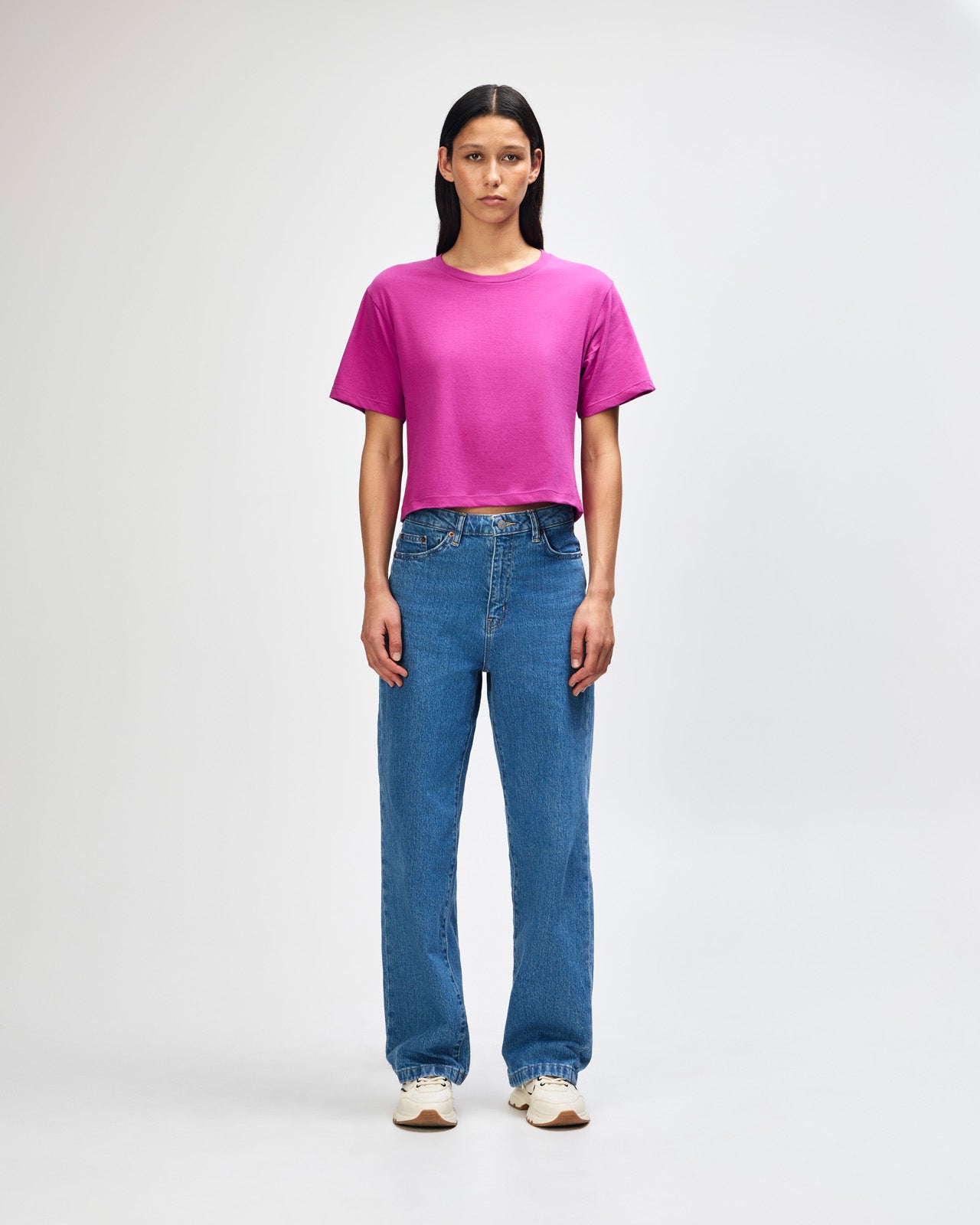 Female model wearing an American Apparel Fine Jersey Women's Boxy Tee in Super Pink, paired with blue jeans, standing against a plain background (front pose) -super pink