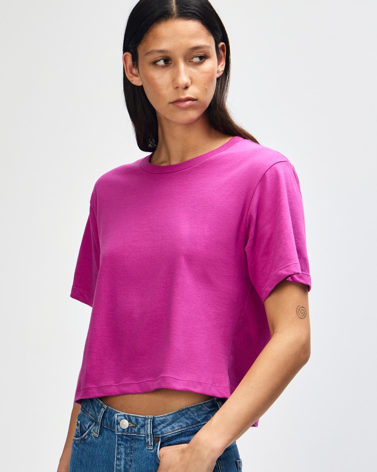 Female model wearing an American Apparel Fine Jersey Women's Boxy Tee in Super Pink, paired with blue jeans, standing against a plain background (front pose) -super pink