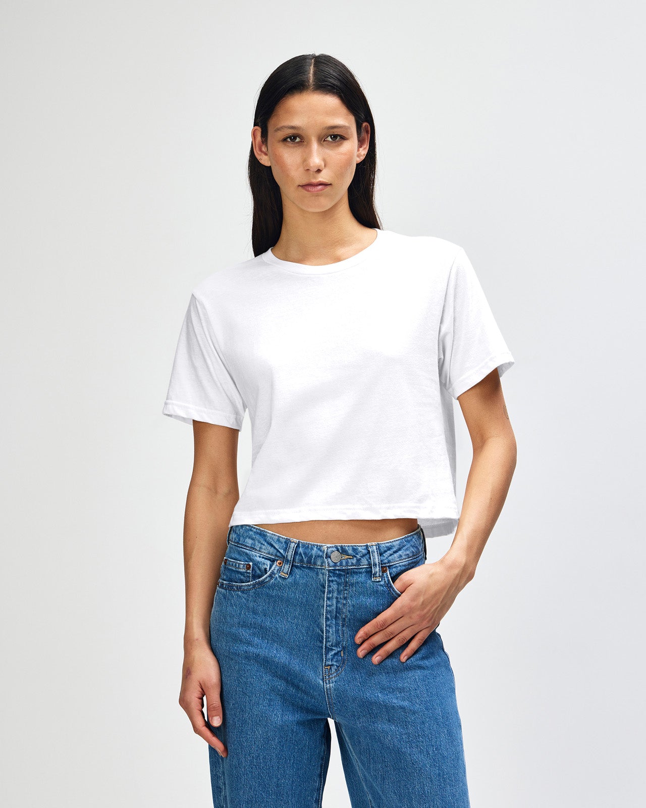 Female model wearing an American Apparel Fine Jersey Women's Boxy Tee in white, paired with blue jeans, standing against a plain background (front pose) -white