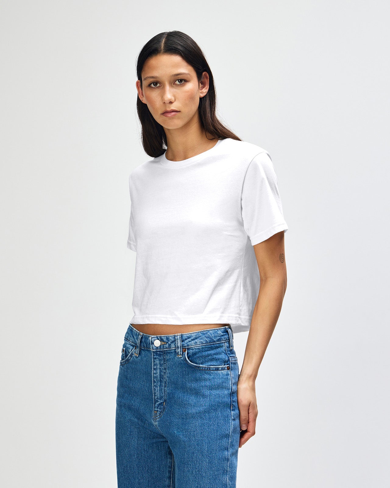 Female model wearing an American Apparel Fine Jersey Women's Boxy Tee in white, paired with blue jeans, standing against a plain background (front pose) -white