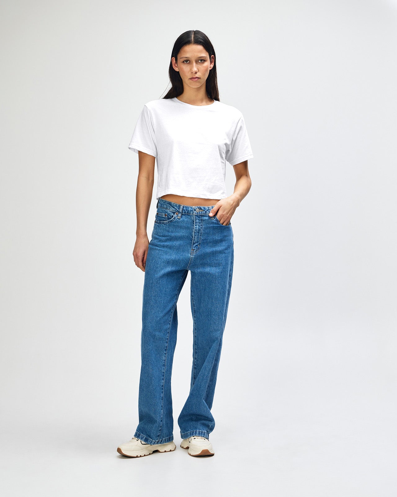 Female model wearing an American Apparel Fine Jersey Women's Boxy Tee in white, paired with blue jeans, standing against a plain background (front pose) -white