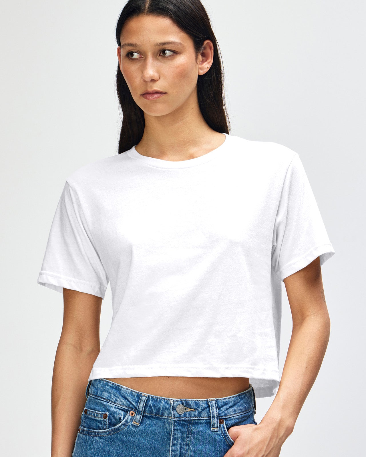 Female model wearing an American Apparel Fine Jersey Women's Boxy Tee in white, paired with blue jeans, standing against a plain background (front pose) -white