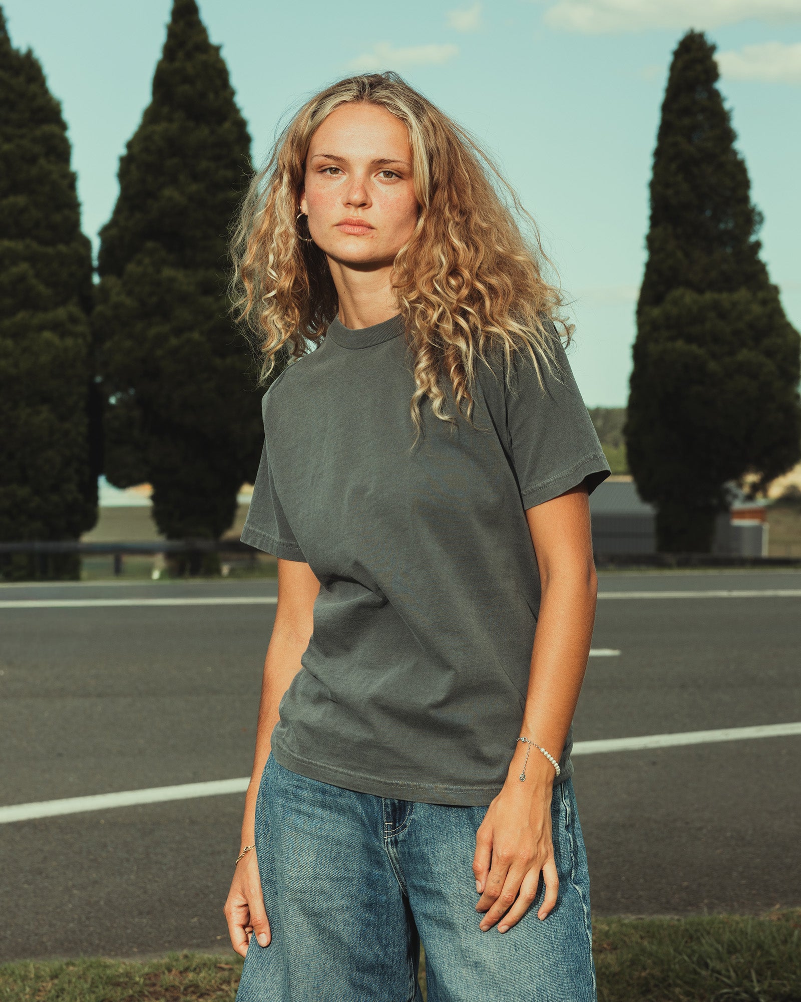 Male model wearing an American Apparel Garment Dyed Heavyweight Cotton Tee Shirt in Faded Black, paired with light blue jeans, standing against a plain background (front pose) -black