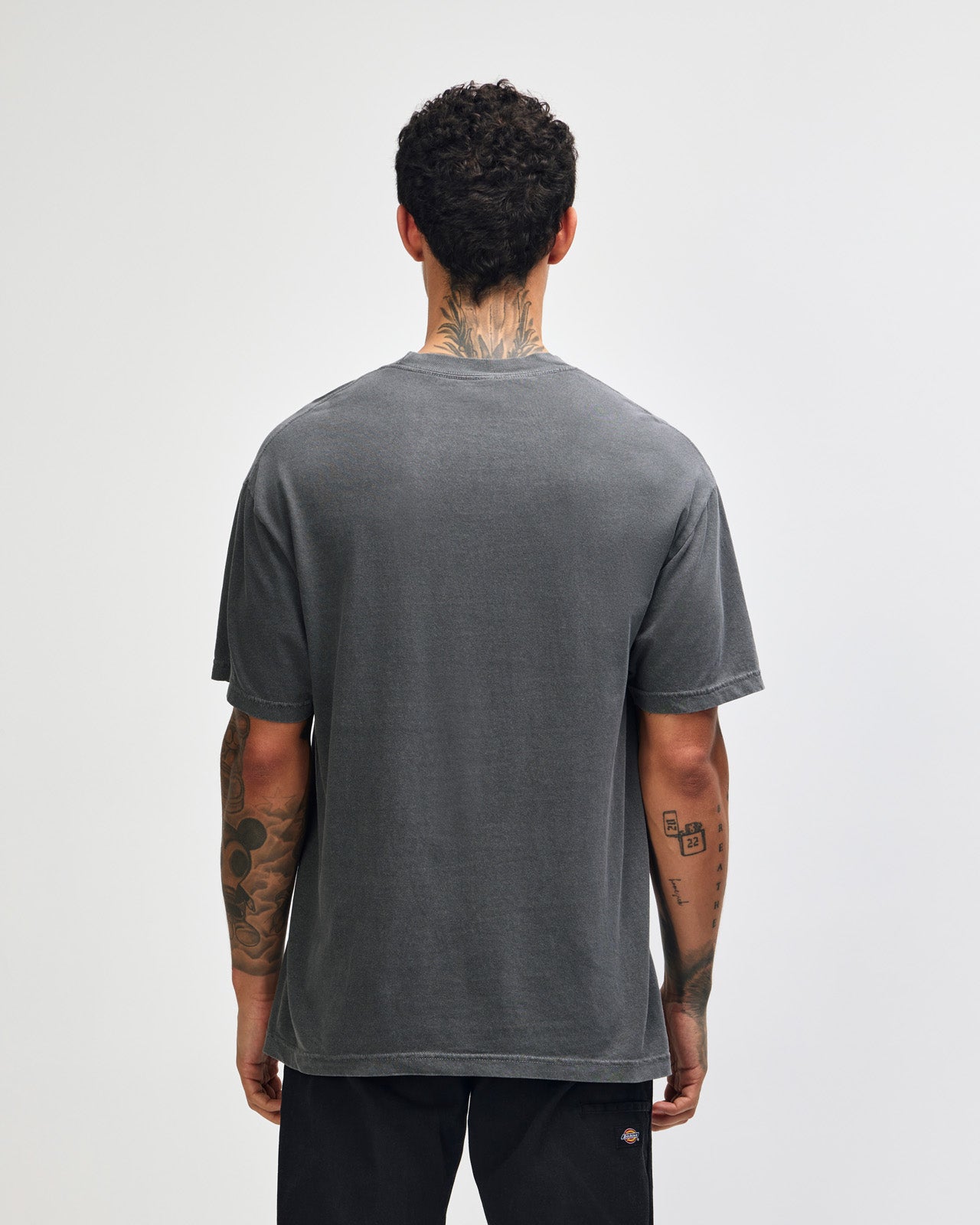 Male model wearing an American Apparel Garment Dyed Heavyweight Cotton Tee Shirt in Faded Black, paired with light blue jeans, standing against a plain background (front pose) -black
