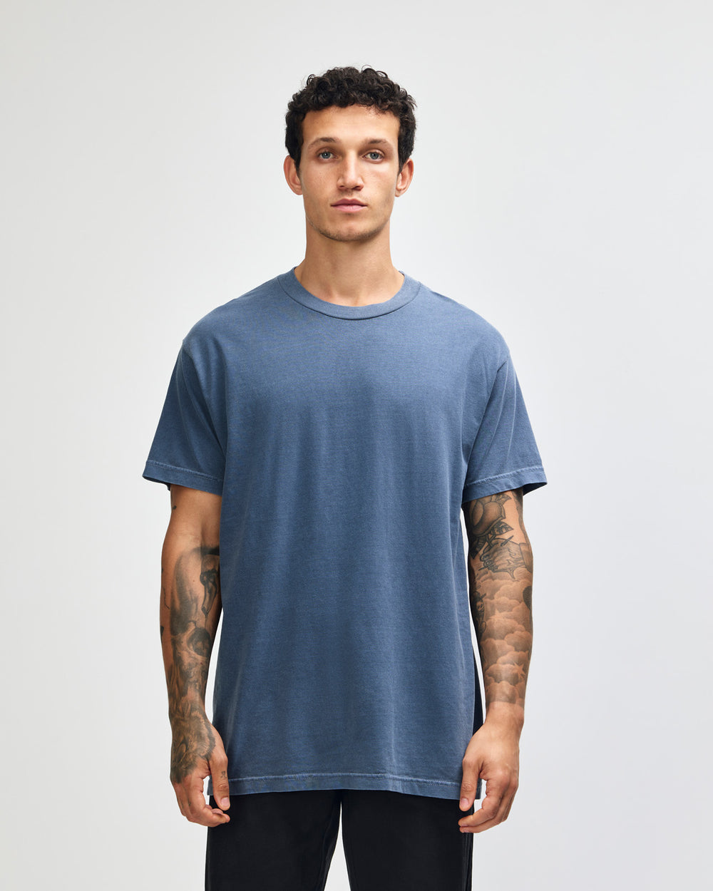 next image of Unisex Faded T-shirt : Male model wearing an American Apparel Garment Dyed Heavyweight Cotton Tee Shirt in Faded Navy, paired with light blue jeans, standing against a plain background (front pose) -Navy