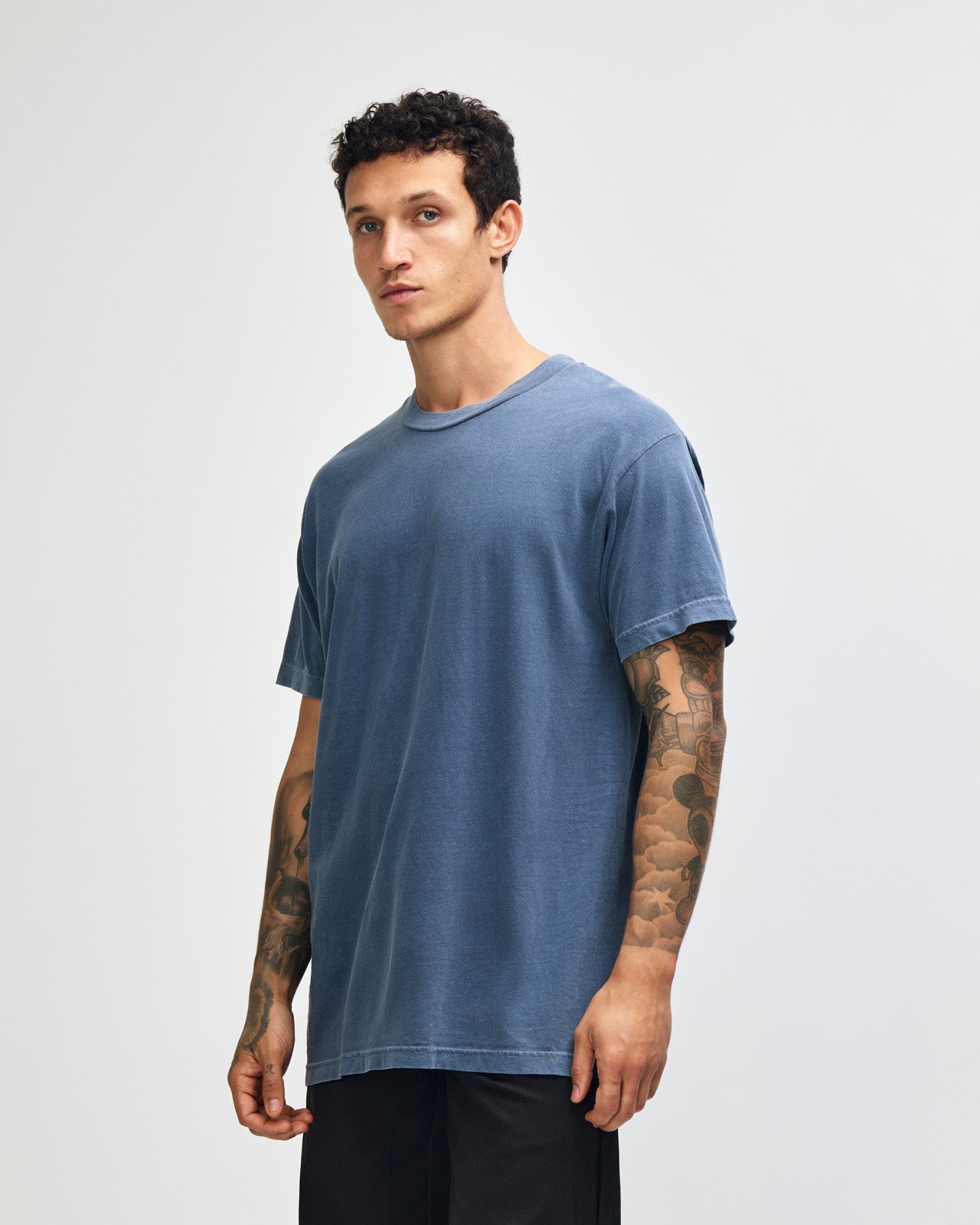 Male model wearing an American Apparel Garment Dyed Heavyweight Cotton Tee Shirt in Faded Navy, paired with light blue jeans, standing against a plain background (front pose) -Navy