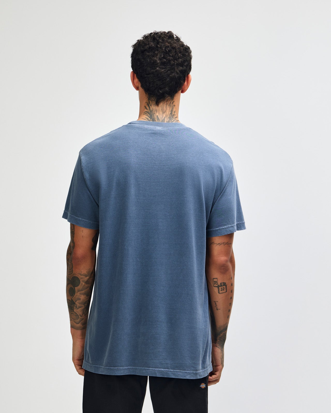 Male model wearing an American Apparel Garment Dyed Heavyweight Cotton Tee Shirt in Faded Navy, paired with light blue jeans, standing against a plain background (front pose) -Navy