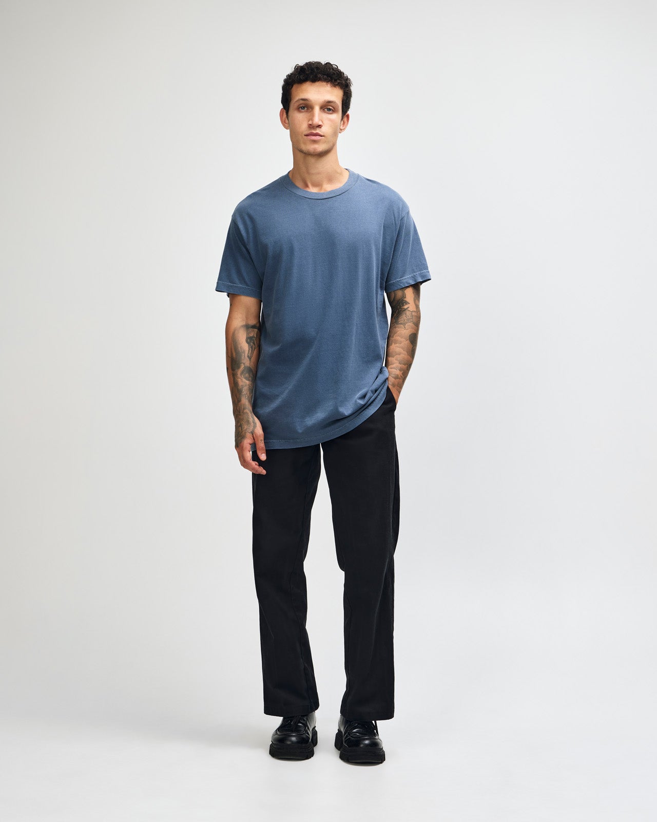 Male model wearing an American Apparel Garment Dyed Heavyweight Cotton Tee Shirt in Faded Navy, paired with light blue jeans, standing against a plain background (front pose) -Navy