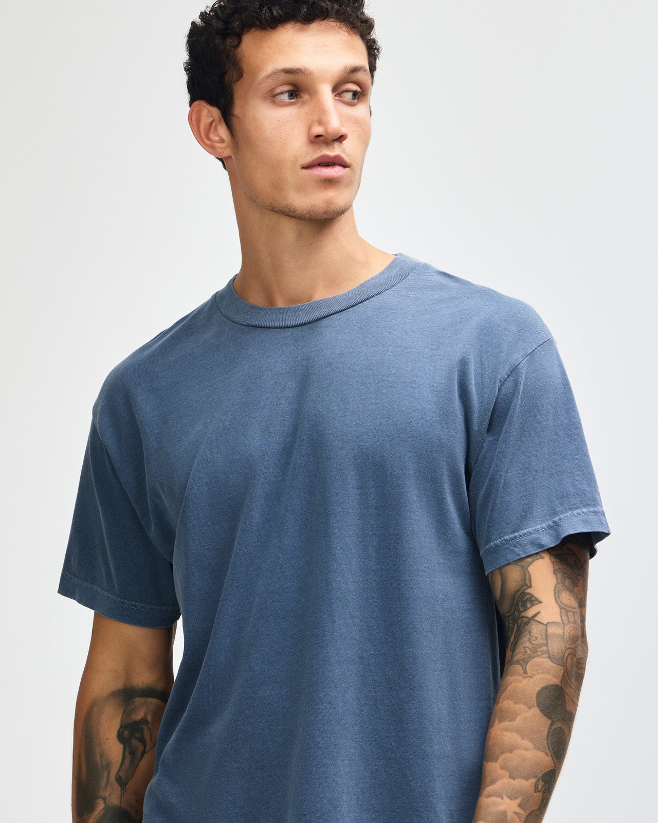 Male model wearing an American Apparel Garment Dyed Heavyweight Cotton Tee Shirt in Faded Navy, paired with light blue jeans, standing against a plain background (front pose) -Navy