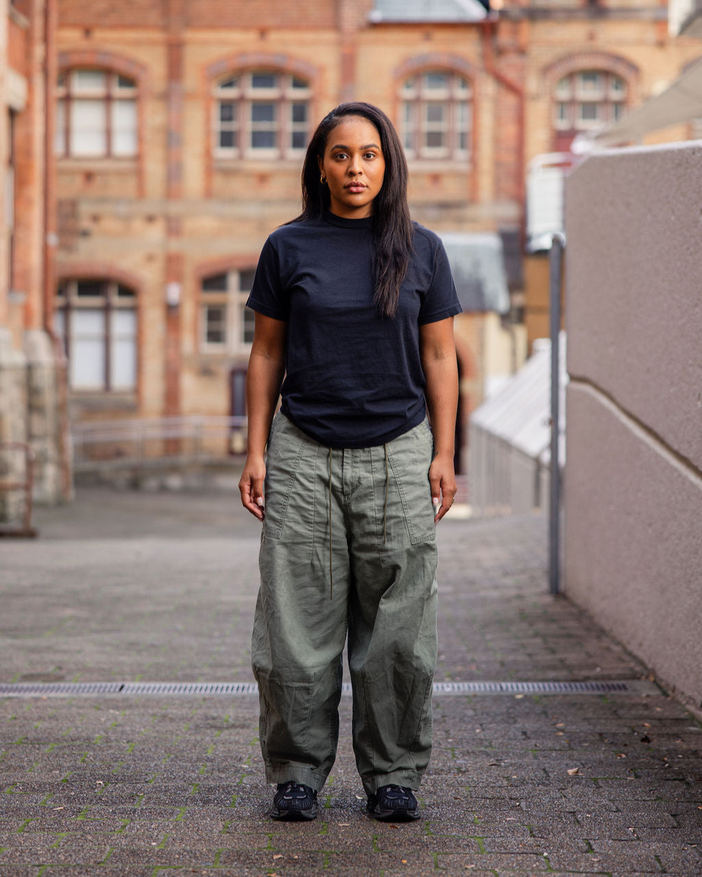 Male model wearing an American Apparel Garment Dyed Heavyweight Cotton Tee Shirt in Faded Brown, paired with light blue jeans, standing against a plain background (front pose) -true black