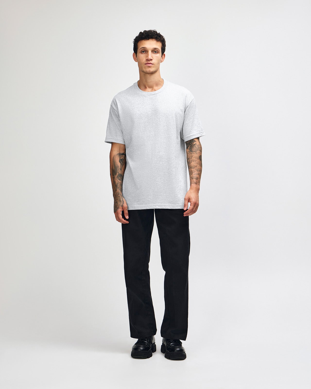 Male Model wearing a Ash Heavyweight Unisex Short Sleeve Crew Neck Tee, paired with green cargo pants standing against a plain background (front pose) -ash