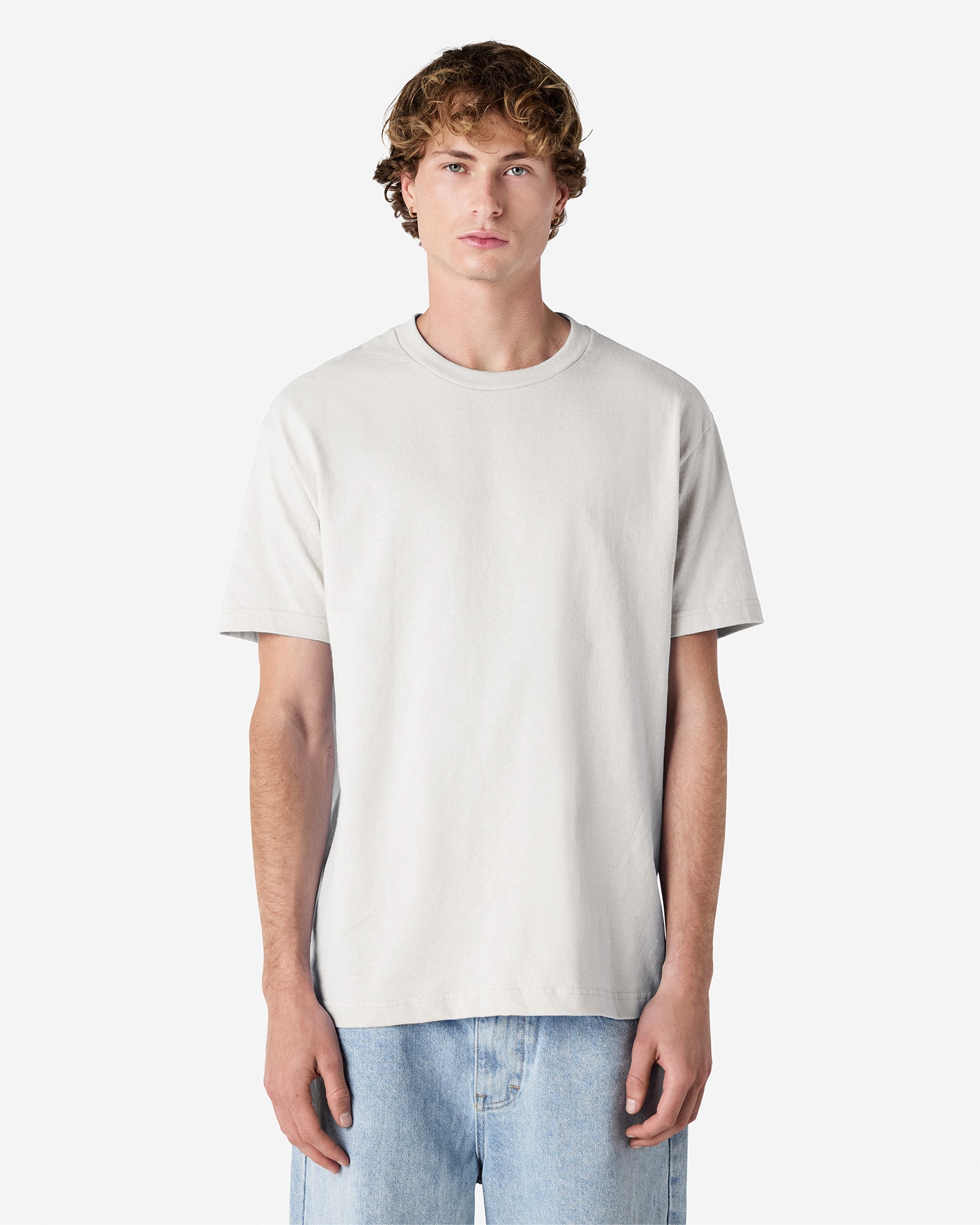 Male Model wearing a Ash Heavyweight Unisex Short Sleeve Crew Neck Tee, paired with blue jeans, standing against a plain background (front pose) -ash