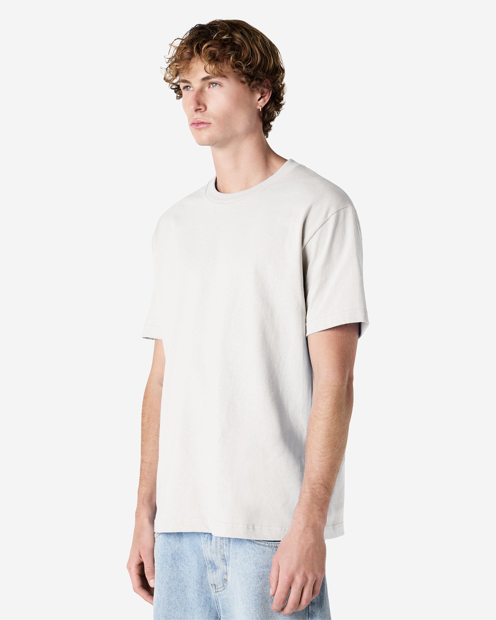 Male Model wearing a Ash Heavyweight Unisex Short Sleeve Crew Neck Tee, paired with blue jeans, standing against a plain background (front pose) -ash
