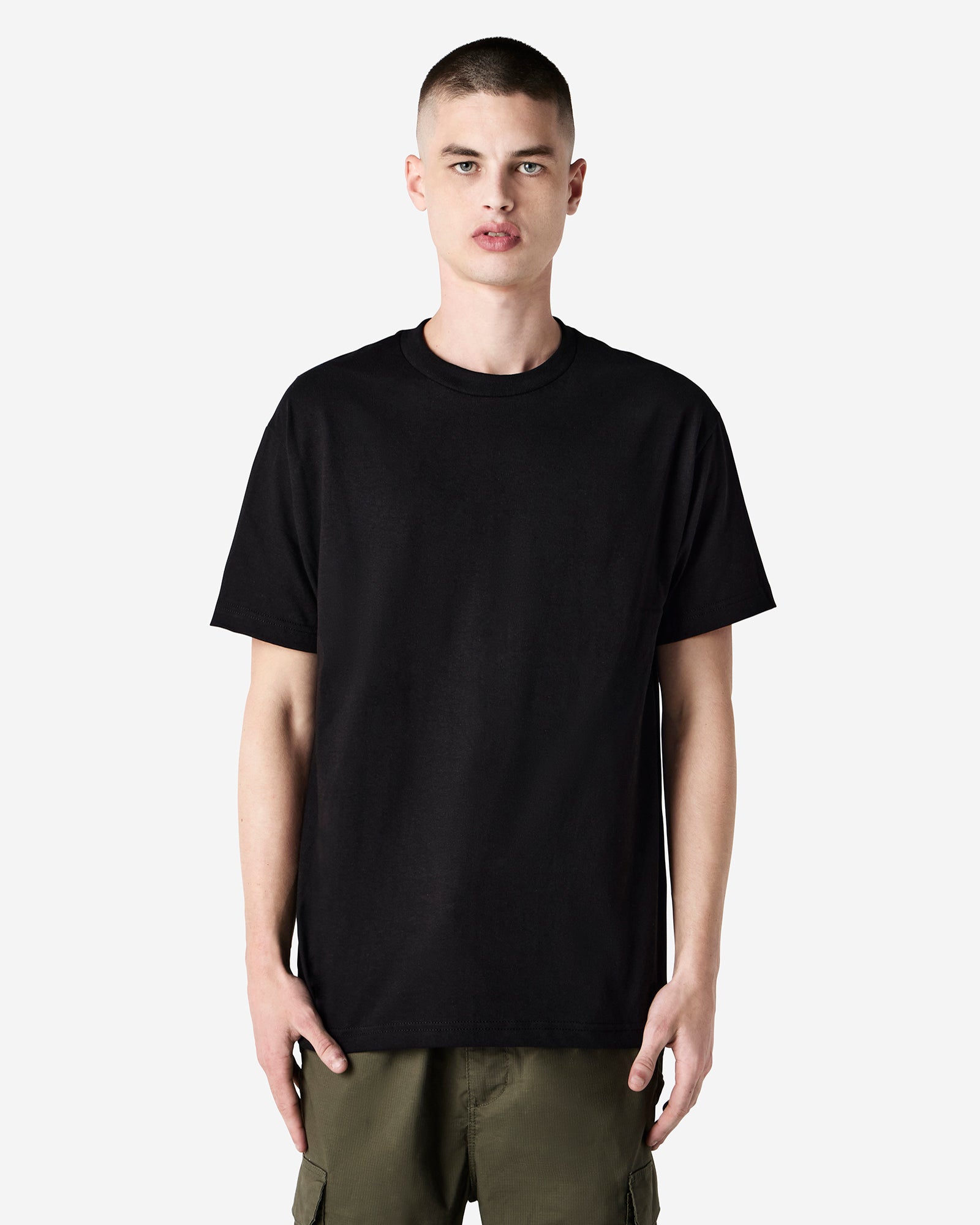 Male Model wearing a black Heavyweight Unisex Short Sleeve Crew Neck Tee, paired with blue jeans, standing against a plain background (front pose) -black