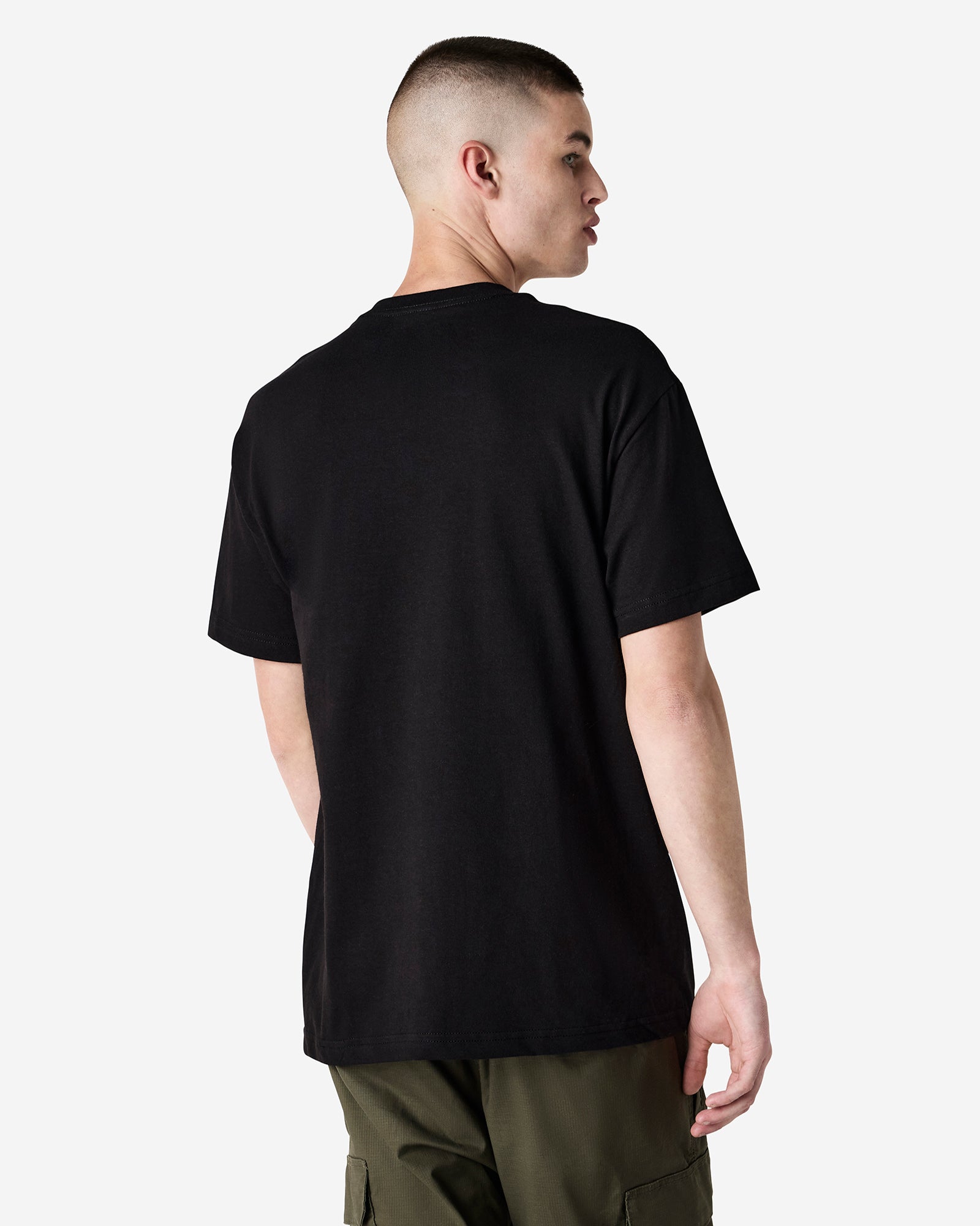 Male Model wearing a Black Heavyweight Unisex Short Sleeve Crew Neck Tee, paired with green jeans, standing against a plain background (back pose) -black