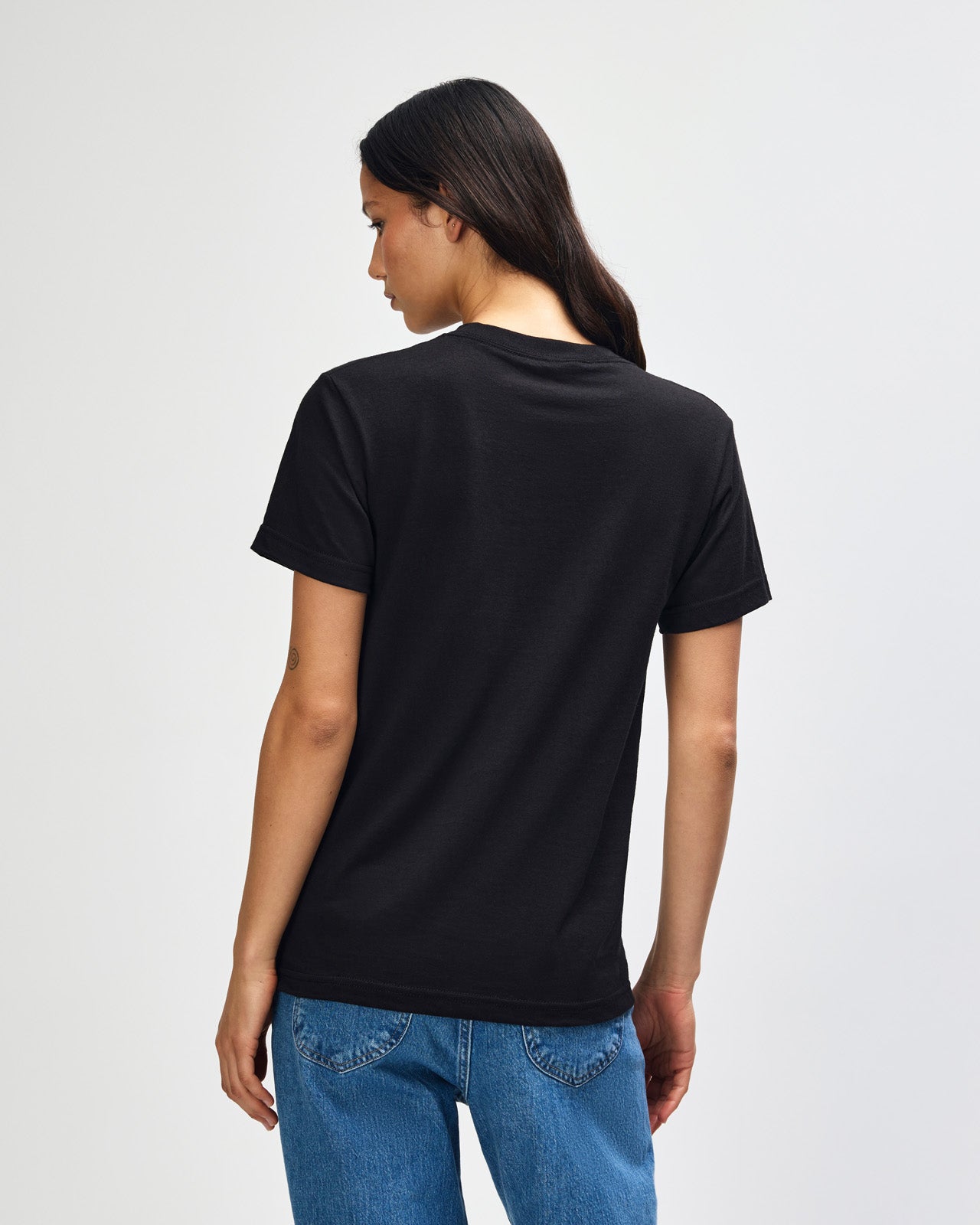 Female Model wearing a black Heavyweight Unisex Short Sleeve Crew Neck Tee, paired with blue jeans, standing against a plain background (front pose) -black