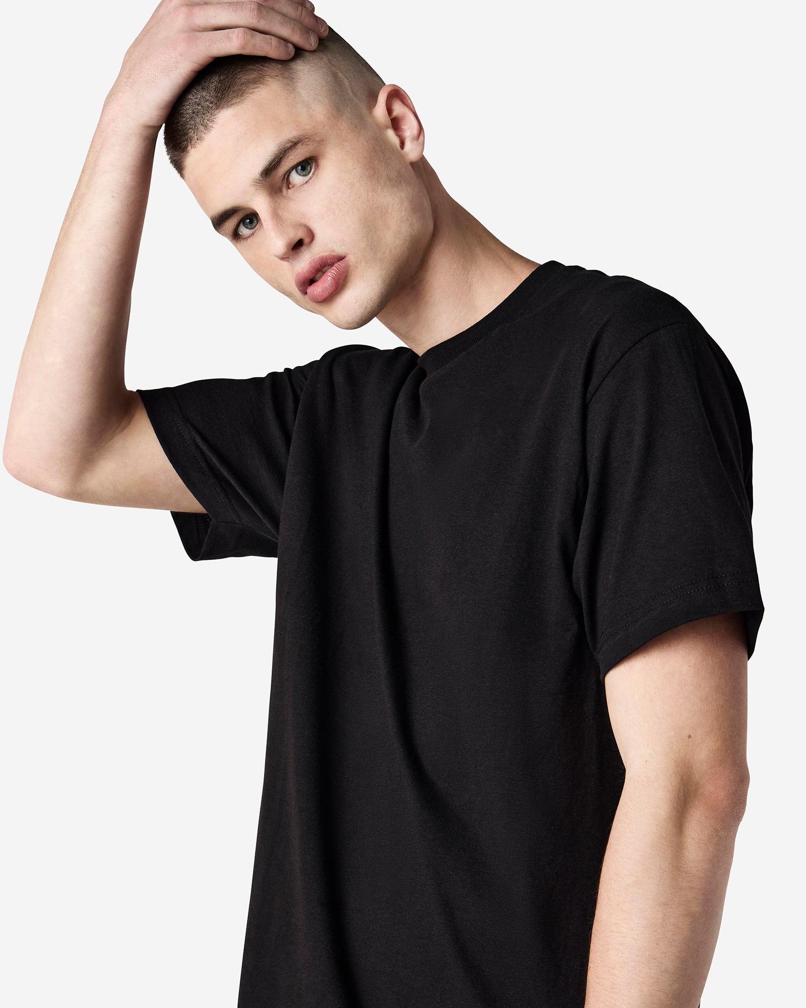 Male Model wearing a Black Heavyweight Unisex Short Sleeve Crew Neck Tee, paired with blue jeans, standing against a plain background (front pose) -black