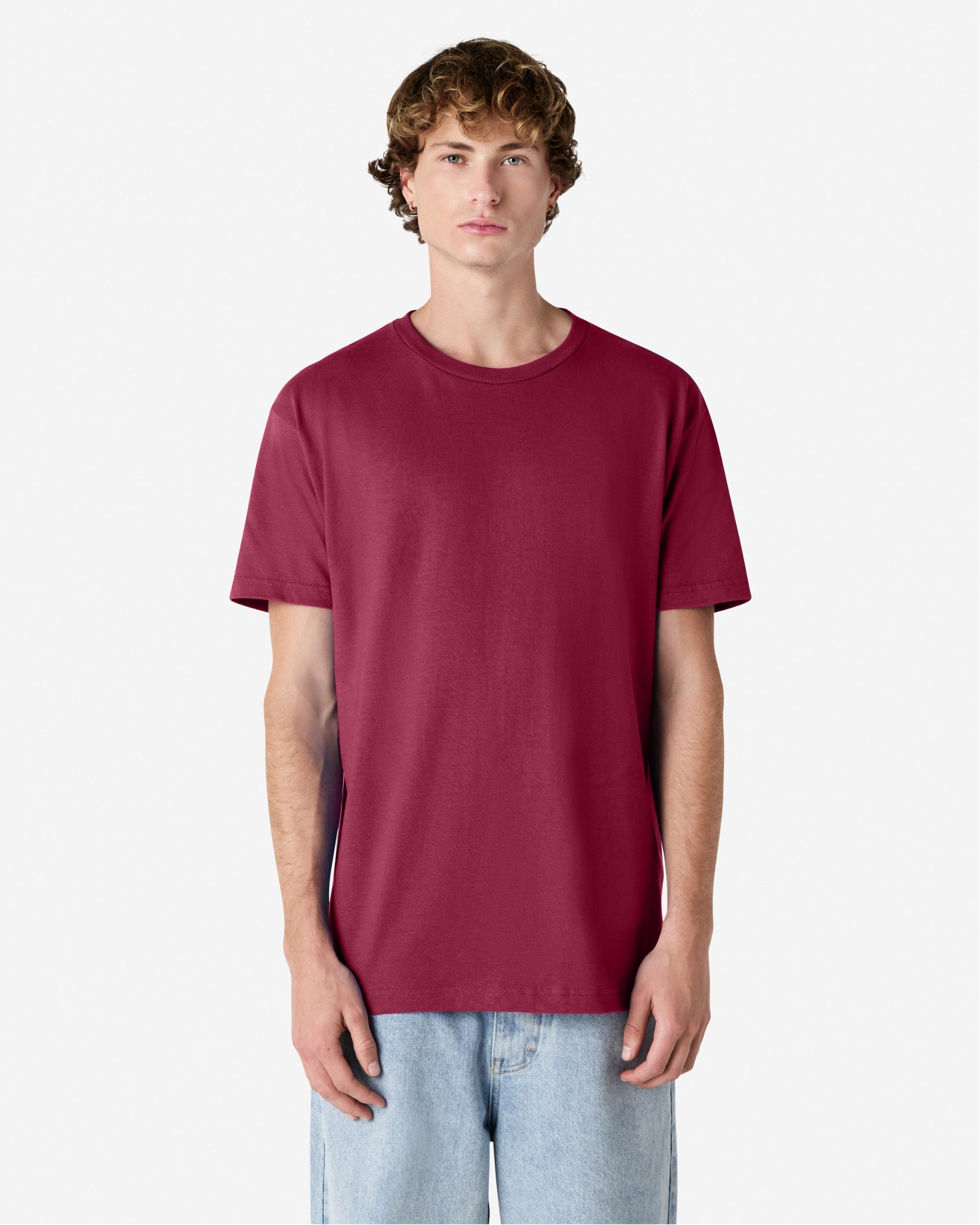 Male Model wearing a Burgundy Heavyweight Unisex Short Sleeve Crew Neck Tee, paired with blue jeans, standing against a plain background (front pose) -burgundy