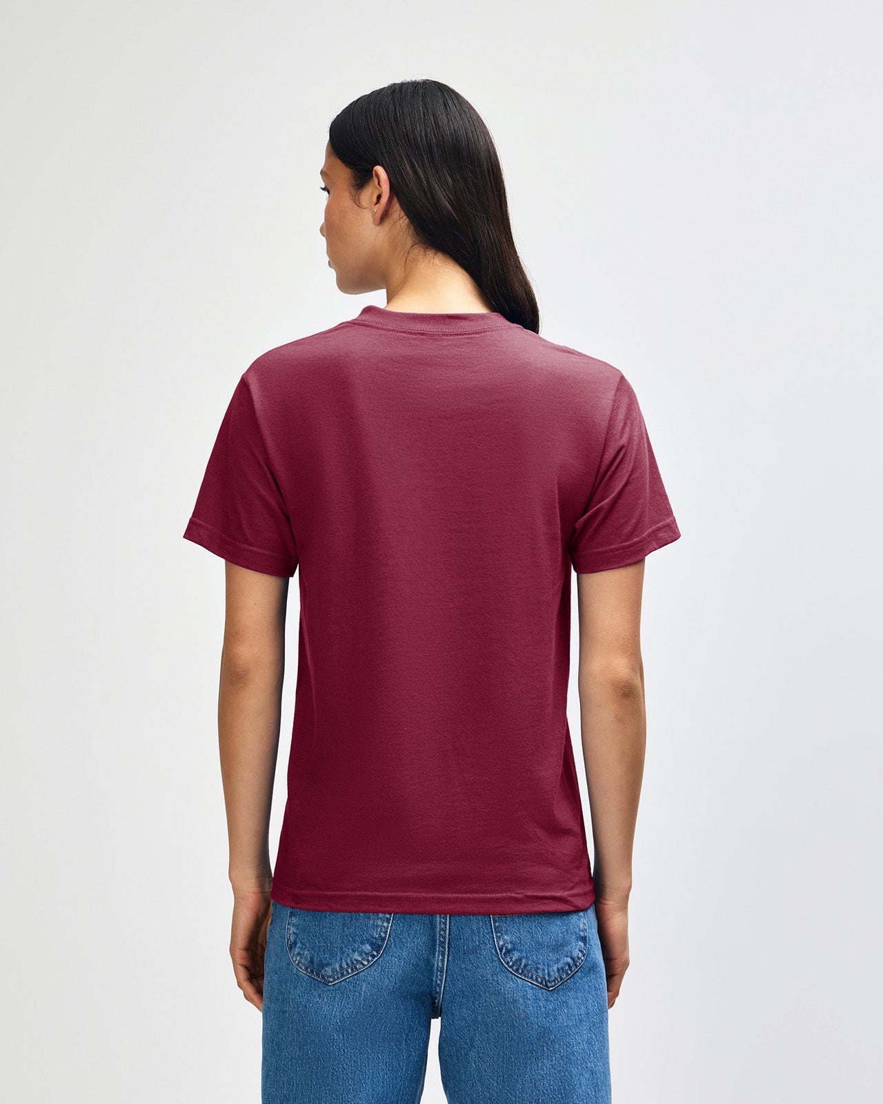 Female Model wearing a Burgundy Heavyweight Unisex Short Sleeve Crew Neck Tee, paired with blue jeans, standing against a plain background (front pose) -burgundy