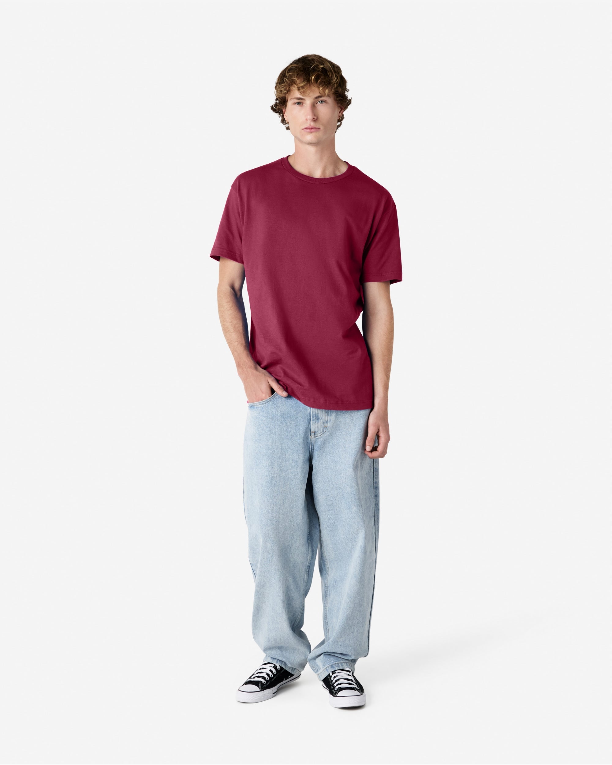 Male Model wearing a Burgundy Heavyweight Unisex Short Sleeve Crew Neck Tee, paired with blue jeans, standing against a plain background (front pose) -burgundy