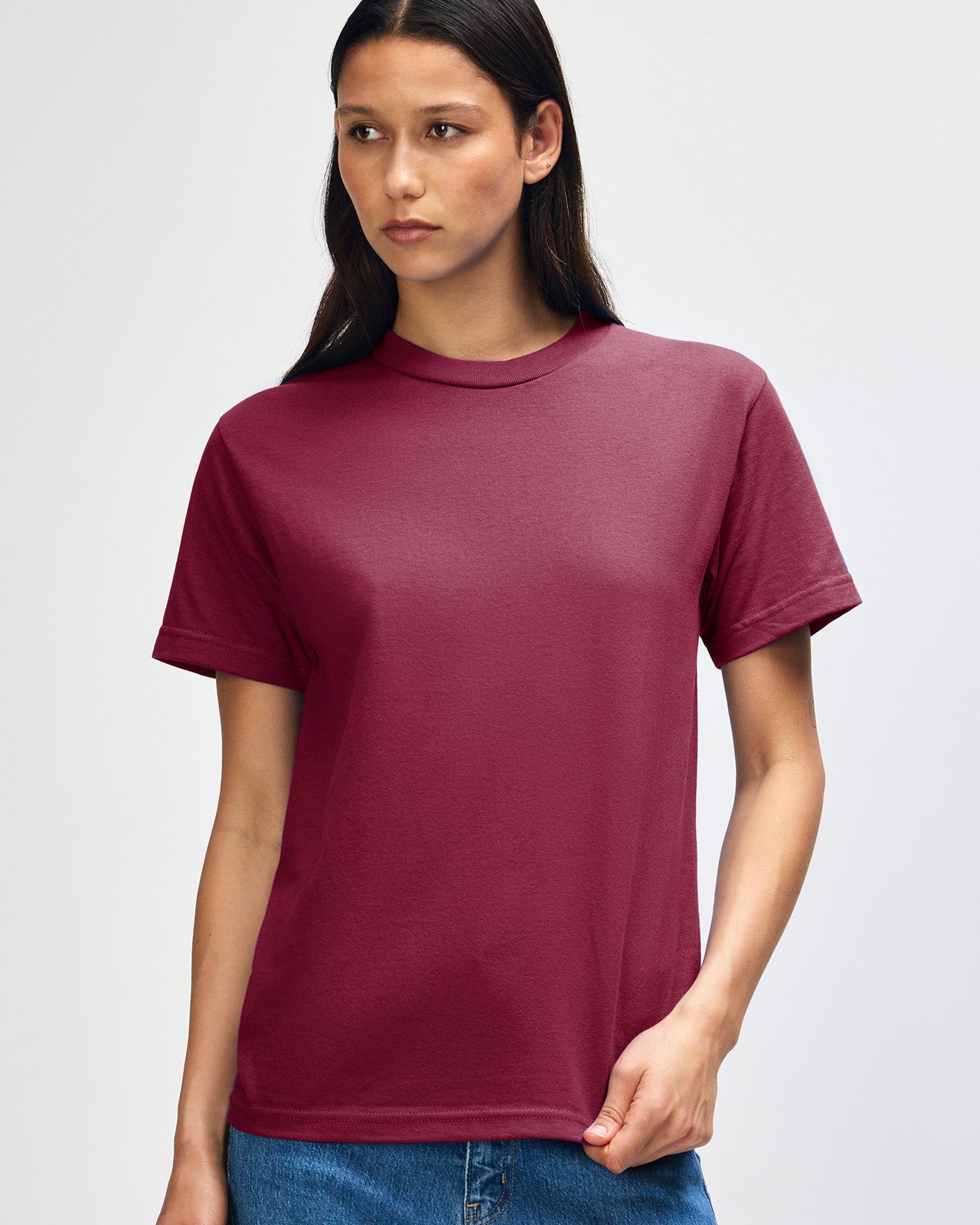 Female Model wearing a Burgundy Heavyweight Unisex Short Sleeve Crew Neck Tee, paired with blue jeans, standing against a plain background (front pose) -burgundy