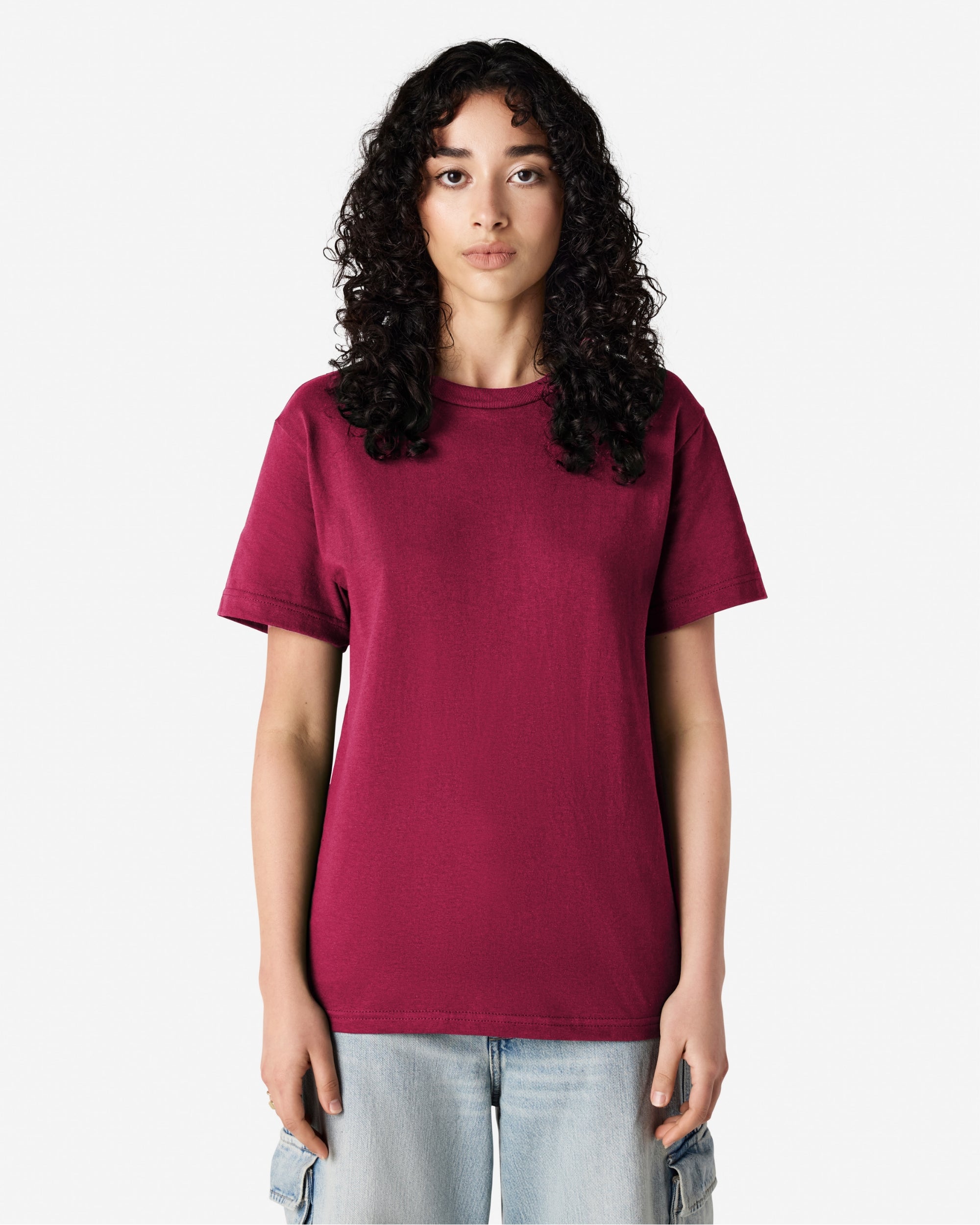 Female Model wearing a Burgundy Heavyweight Unisex Short Sleeve Crew Neck Tee, paired with blue jeans, standing against a plain background (front pose) -burgundy