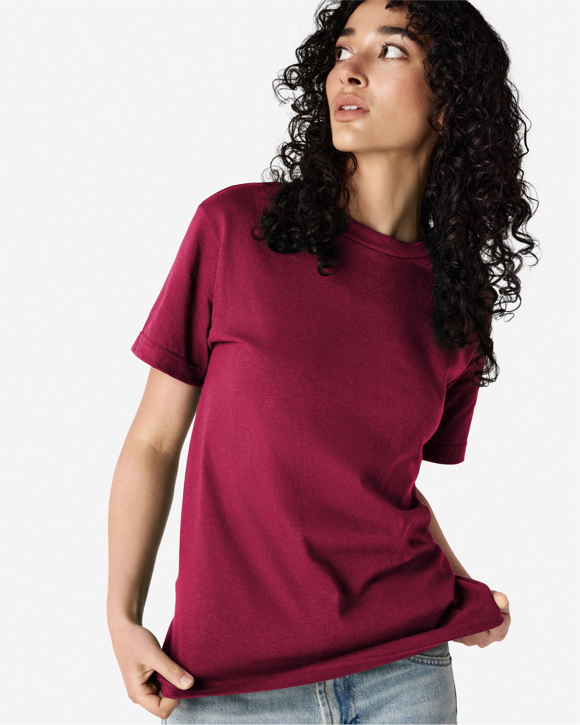 Female Model wearing a Burgundy Heavyweight Unisex Short Sleeve Crew Neck Tee, paired with blue jeans, standing against a plain background (front pose) -burgundy