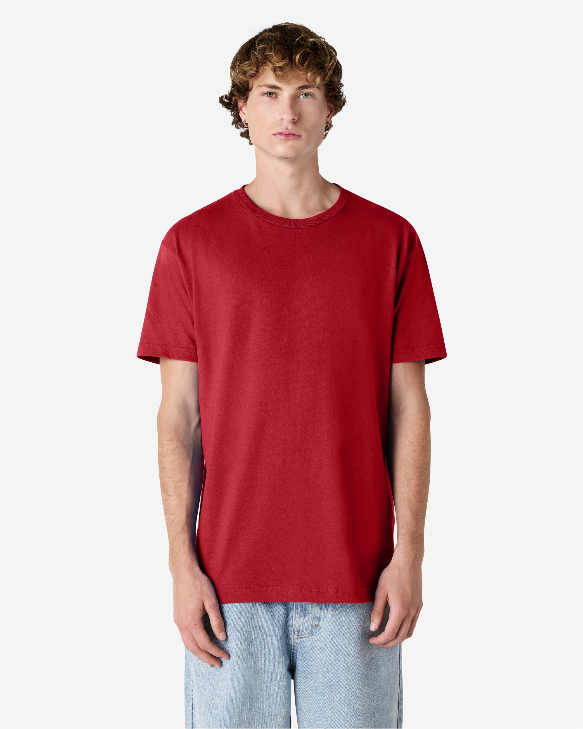 Male Model wearing a Cardinal Heavyweight Unisex Short Sleeve Crew Neck Tee, paired with blue jeans, standing against a plain background (front pose) -cardinal red
