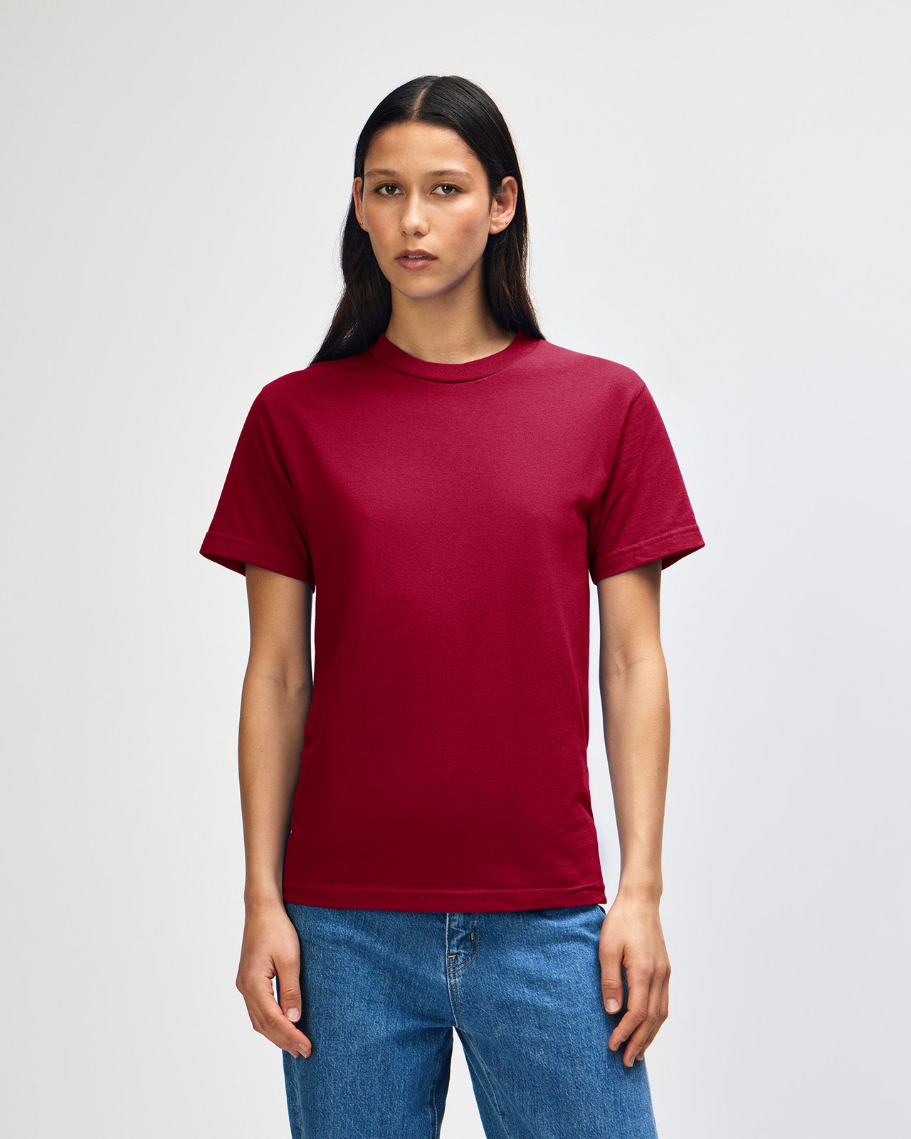 Female Model wearing a Cardinal Heavyweight Unisex Short Sleeve Crew Neck Tee, paired with blue jeans, standing against a plain background (back pose) -cardinal red 