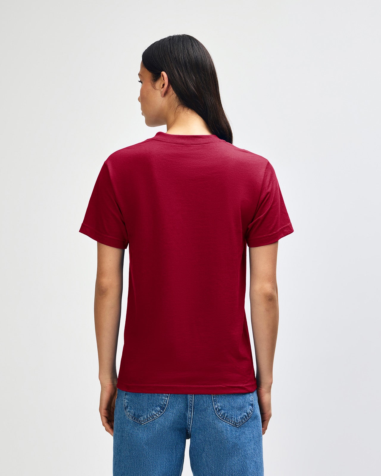 Female Model wearing a Cardinal Heavyweight Unisex Short Sleeve Crew Neck Tee, paired with blue jeans, standing against a plain background (back pose) -cardinal red 