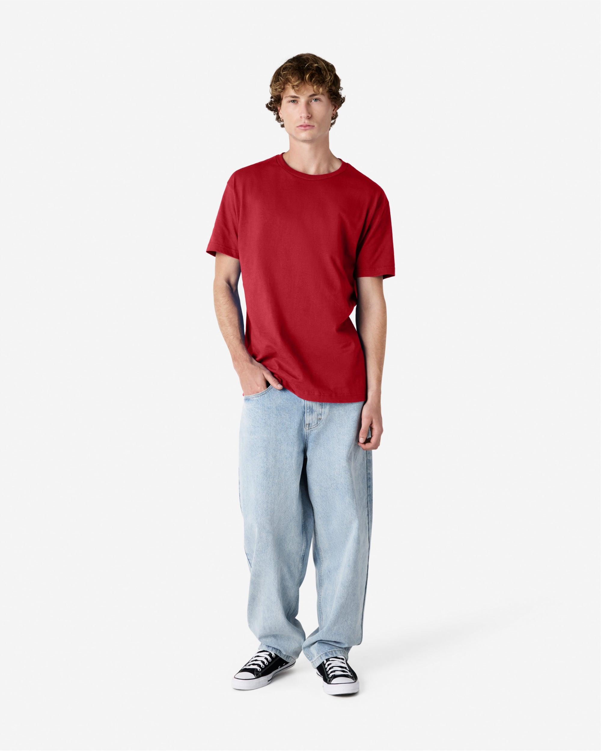 Male Model wearing a Cardinal Heavyweight Unisex Short Sleeve Crew Neck Tee, paired with blue jeans, standing against a plain background (front pose) -cardinal red