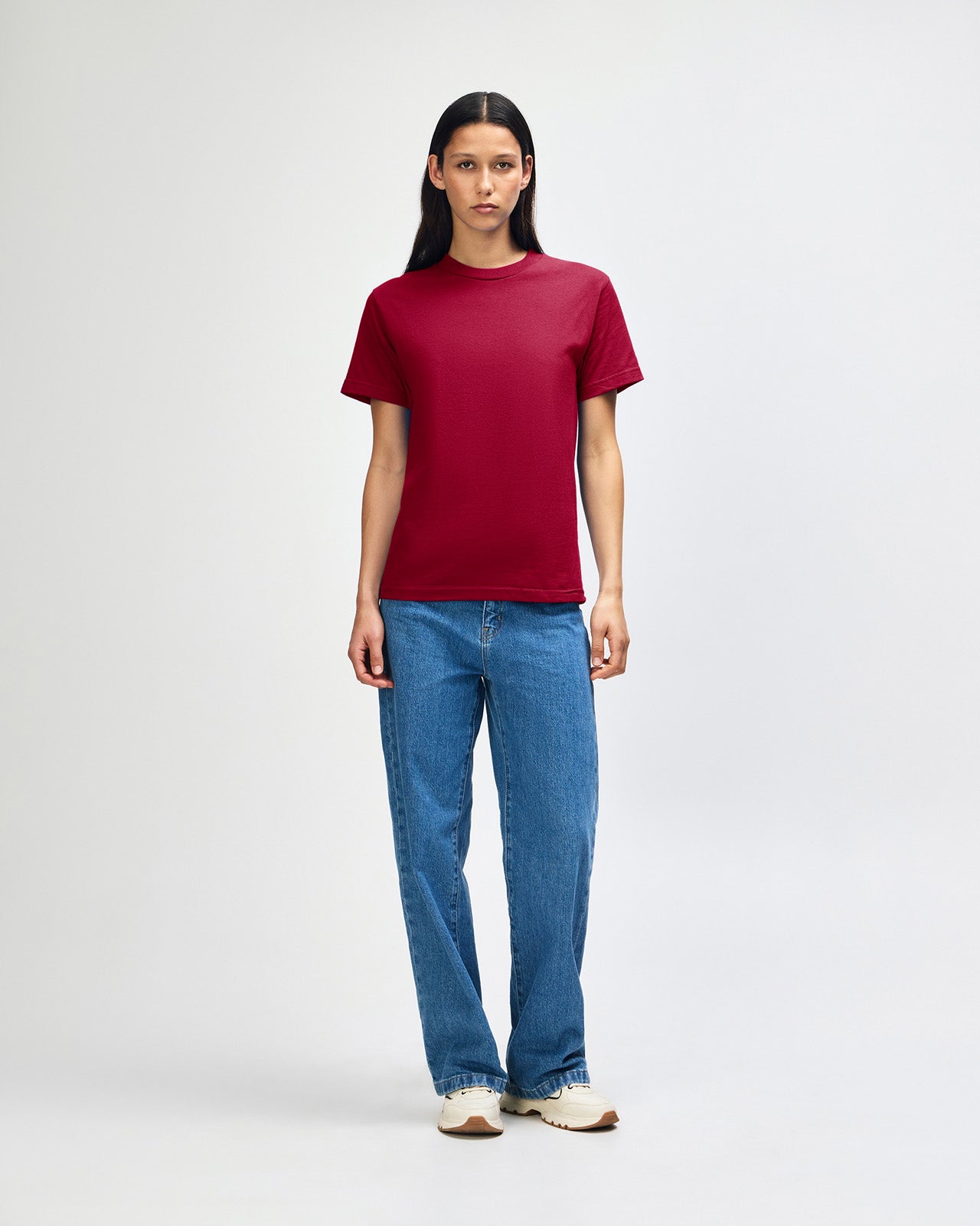 Female Model wearing a Cardinal Heavyweight Unisex Short Sleeve Crew Neck Tee, paired with blue jeans, standing against a plain background (back pose) -cardinal red 