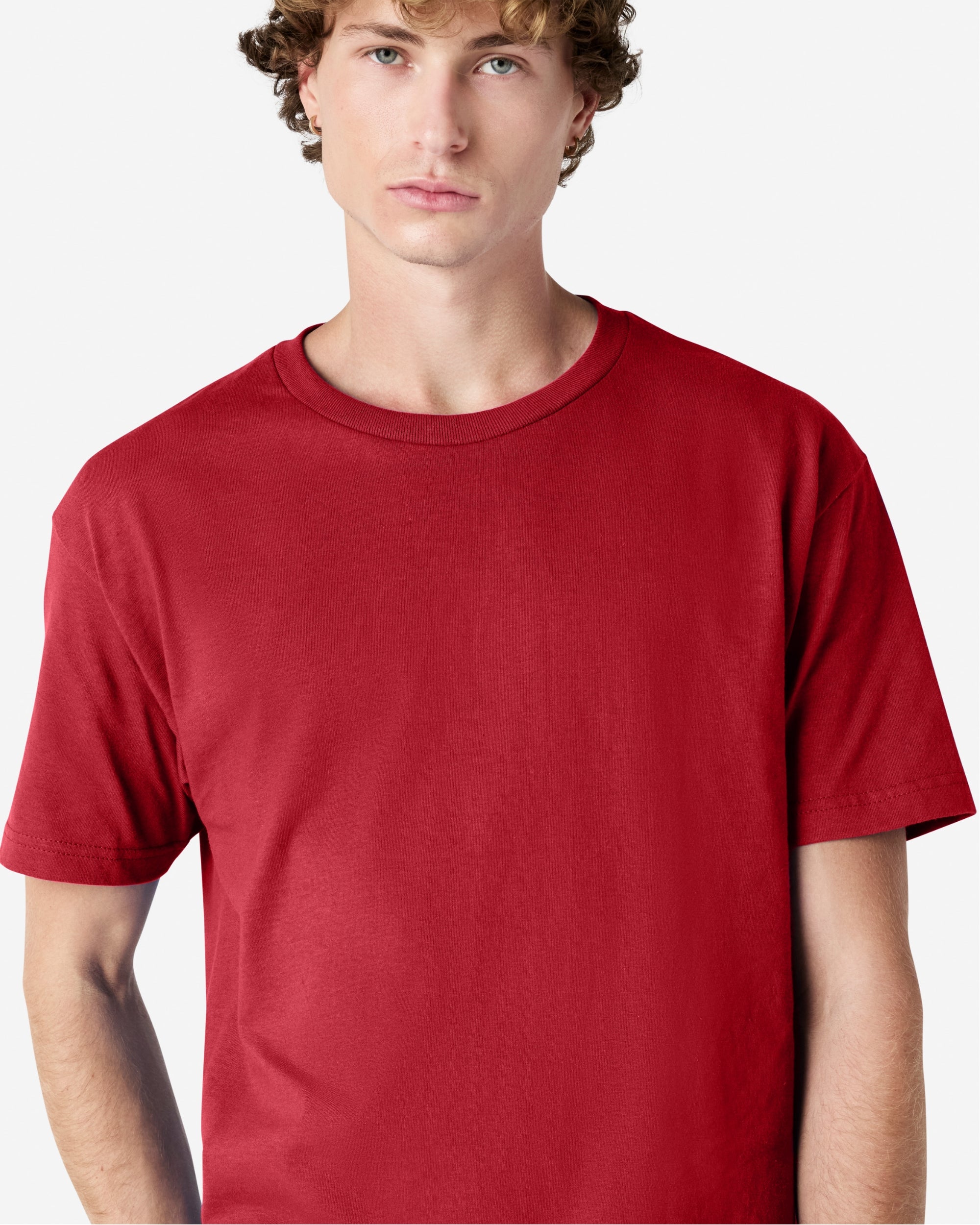 Male Model wearing a Cardinal Heavyweight Unisex Short Sleeve Crew Neck Tee, paired with blue jeans, standing against a plain background (front pose) -cardinal red