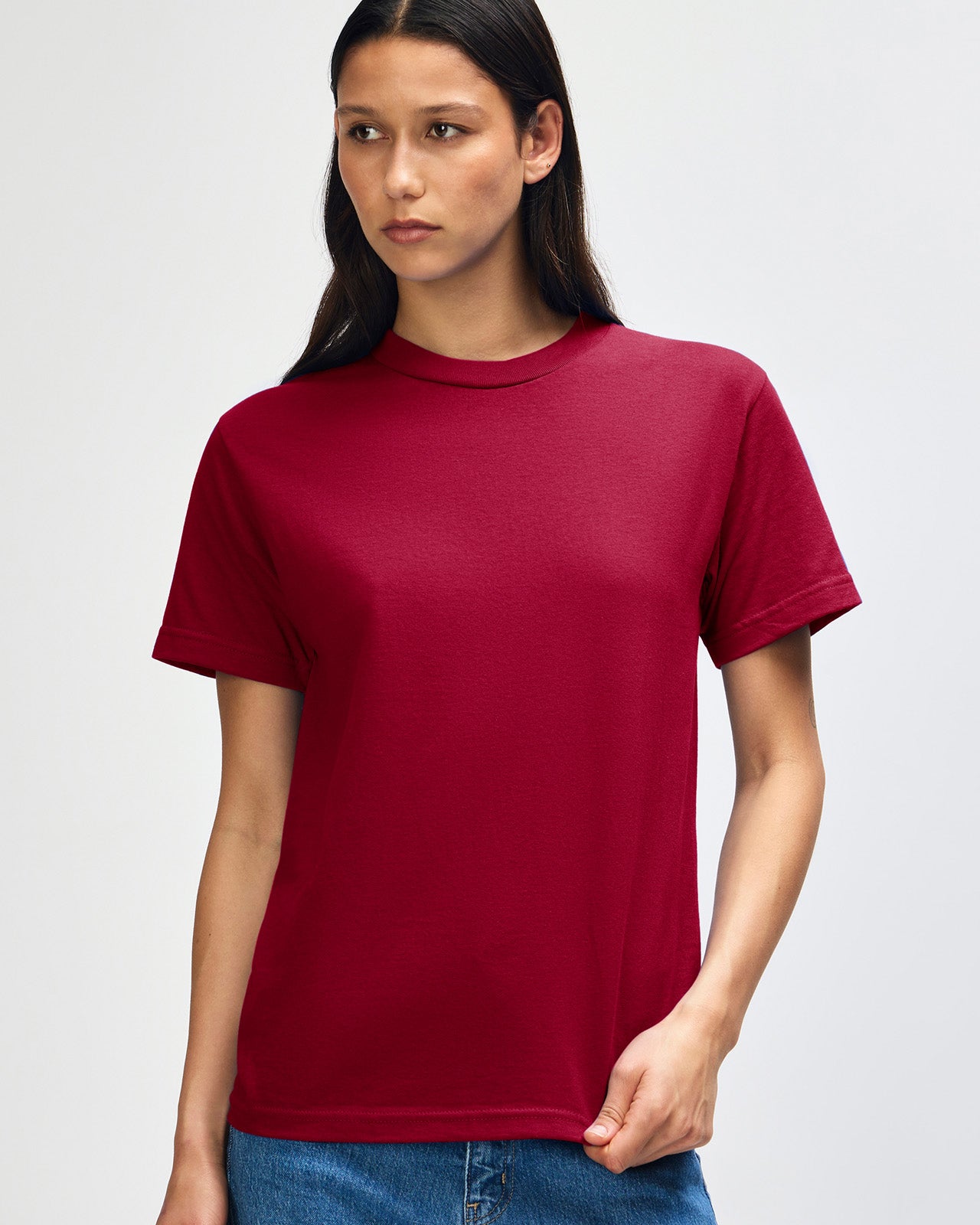 Female Model wearing a Cardinal Heavyweight Unisex Short Sleeve Crew Neck Tee, paired with blue jeans, standing against a plain background (back pose) -cardinal red