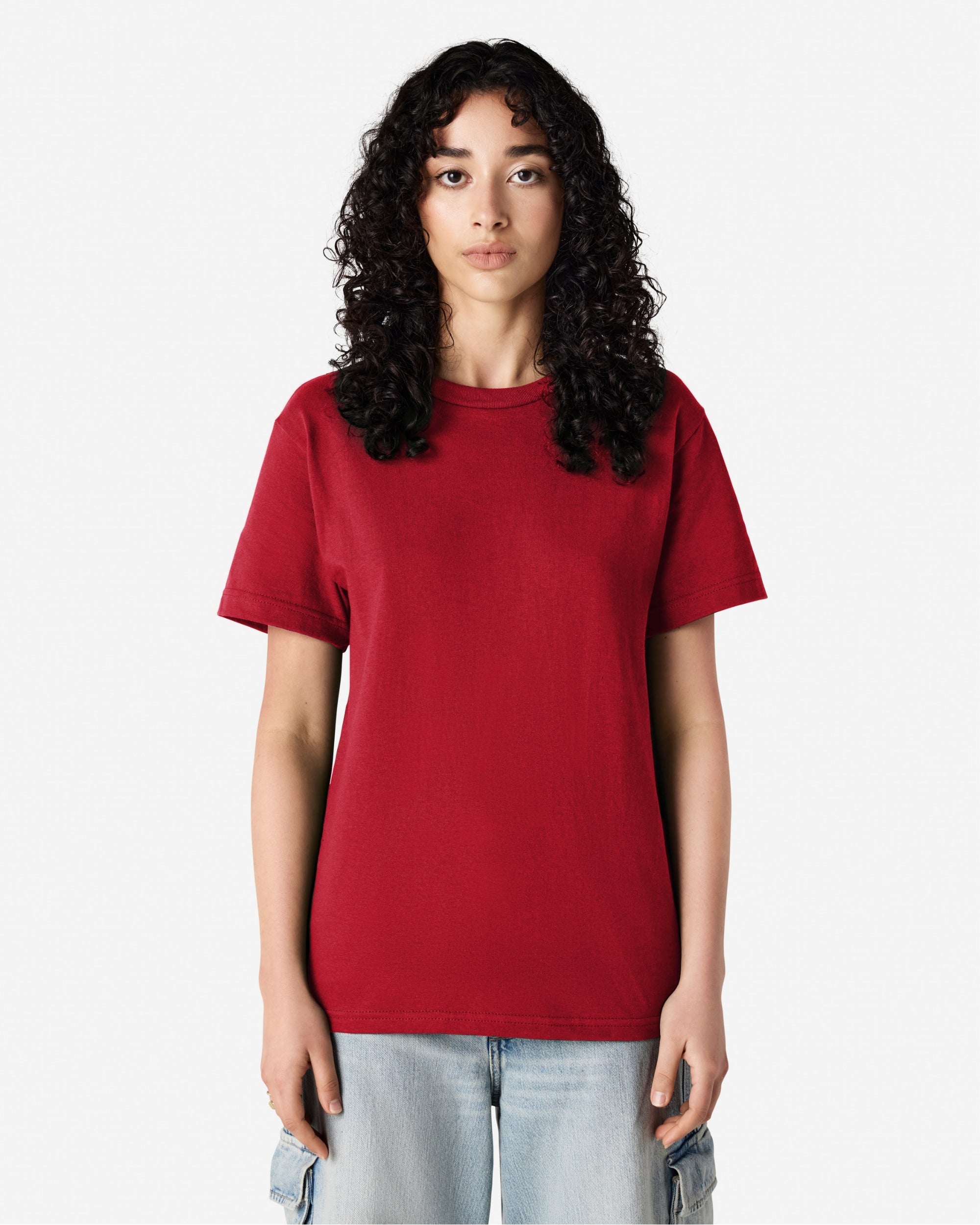Female Model wearing a Cardinal Heavyweight Unisex Short Sleeve Crew Neck Tee, paired with blue jeans, standing against a plain background (back pose) -cardinal red