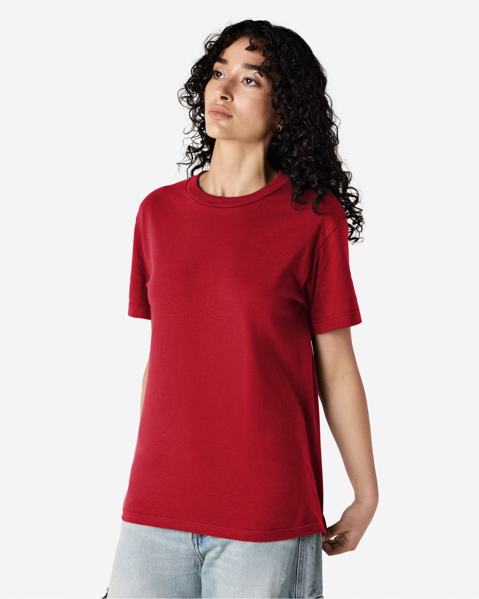 Female Model wearing a red Heavyweight Unisex Short Sleeve Crew Neck Tee, paired with blue jeans, standing against a plain background (front pose) -cardinal red