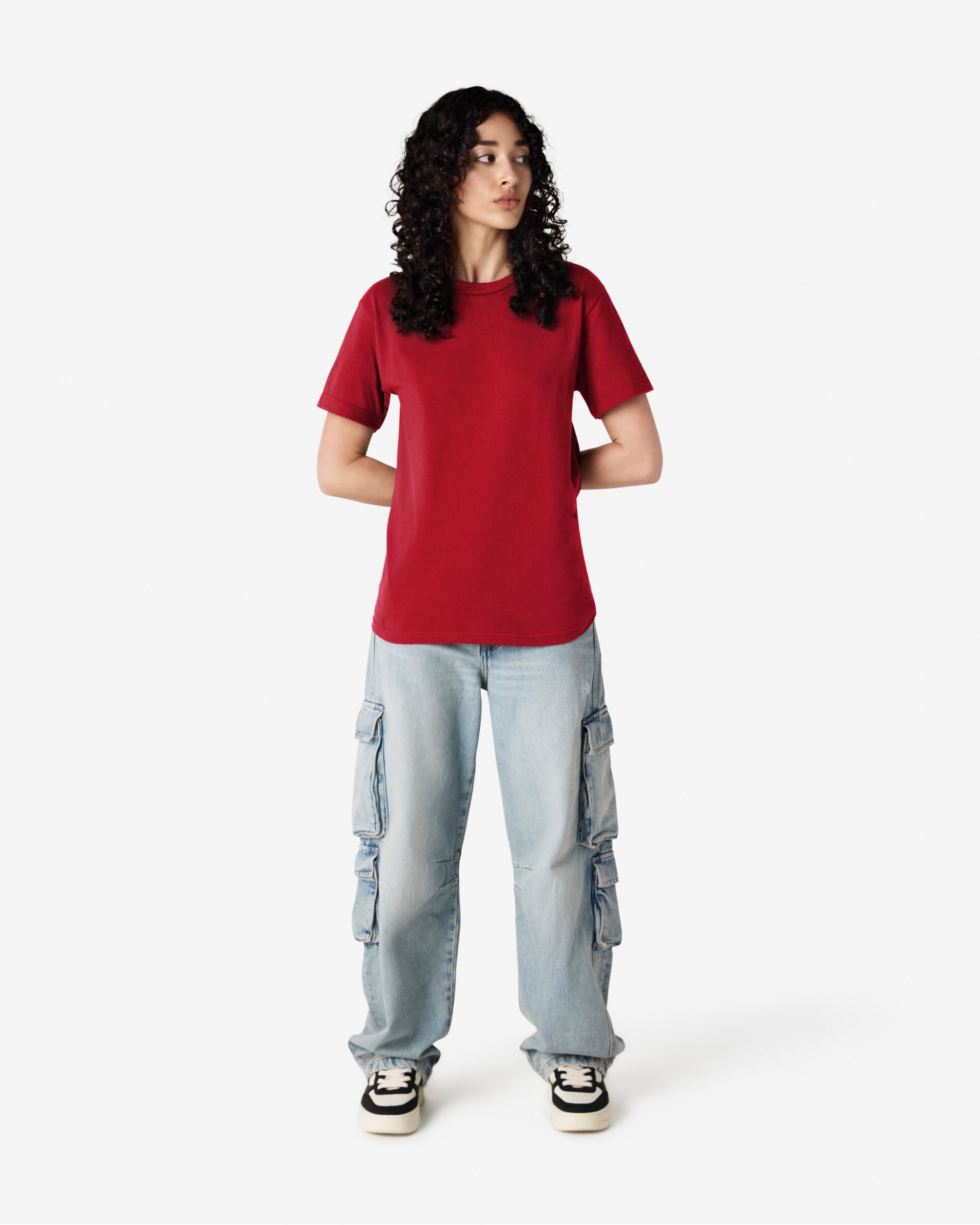 Female Model wearing a Cardinal Heavyweight Unisex Short Sleeve Crew Neck Tee, paired with blue jeans, standing against a plain background (front pose) -cardinal red