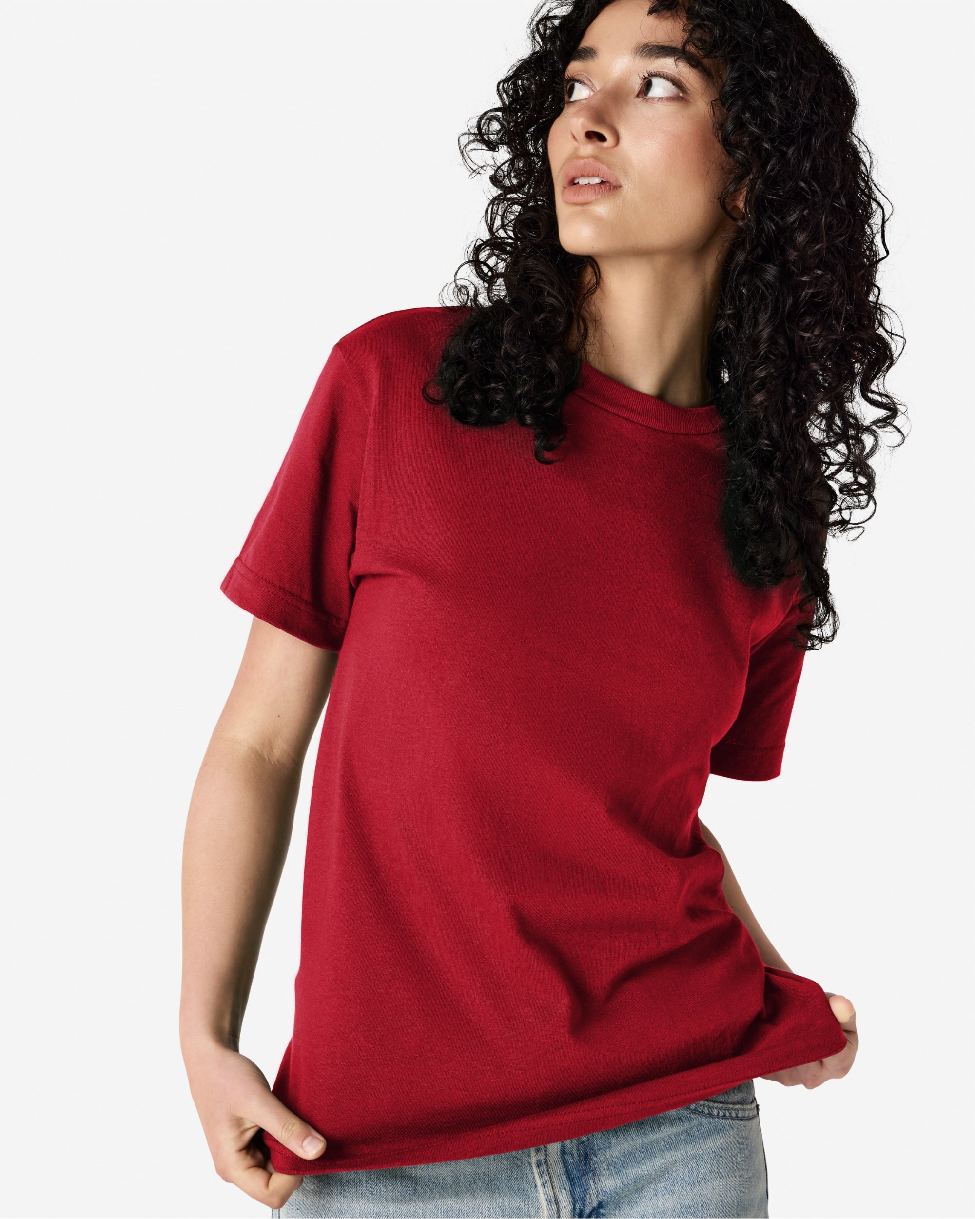 Female Model wearing a Cardinal Heavyweight Unisex Short Sleeve Crew Neck Tee, paired with blue jeans, standing against a plain background (front pose) -cardinal red