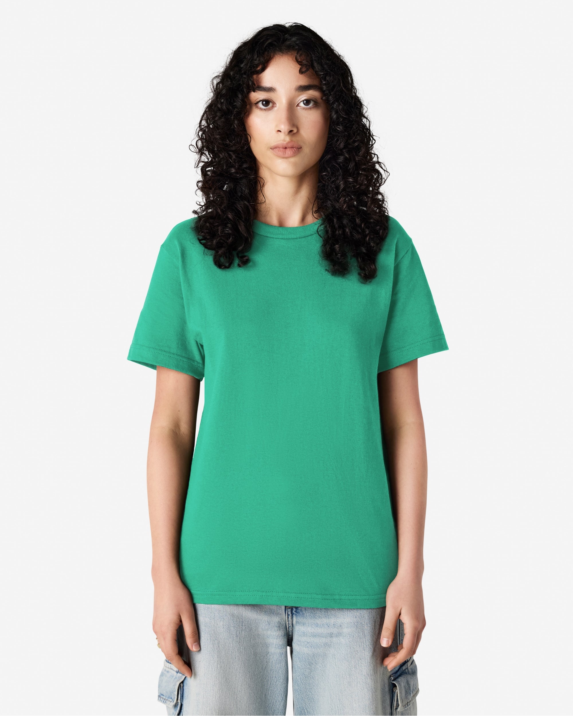 Female Model wearing a Celadon Heavyweight Unisex Short Sleeve Crew Neck Tee, paired with blue jeans, standing against a plain background (front pose) -celadon