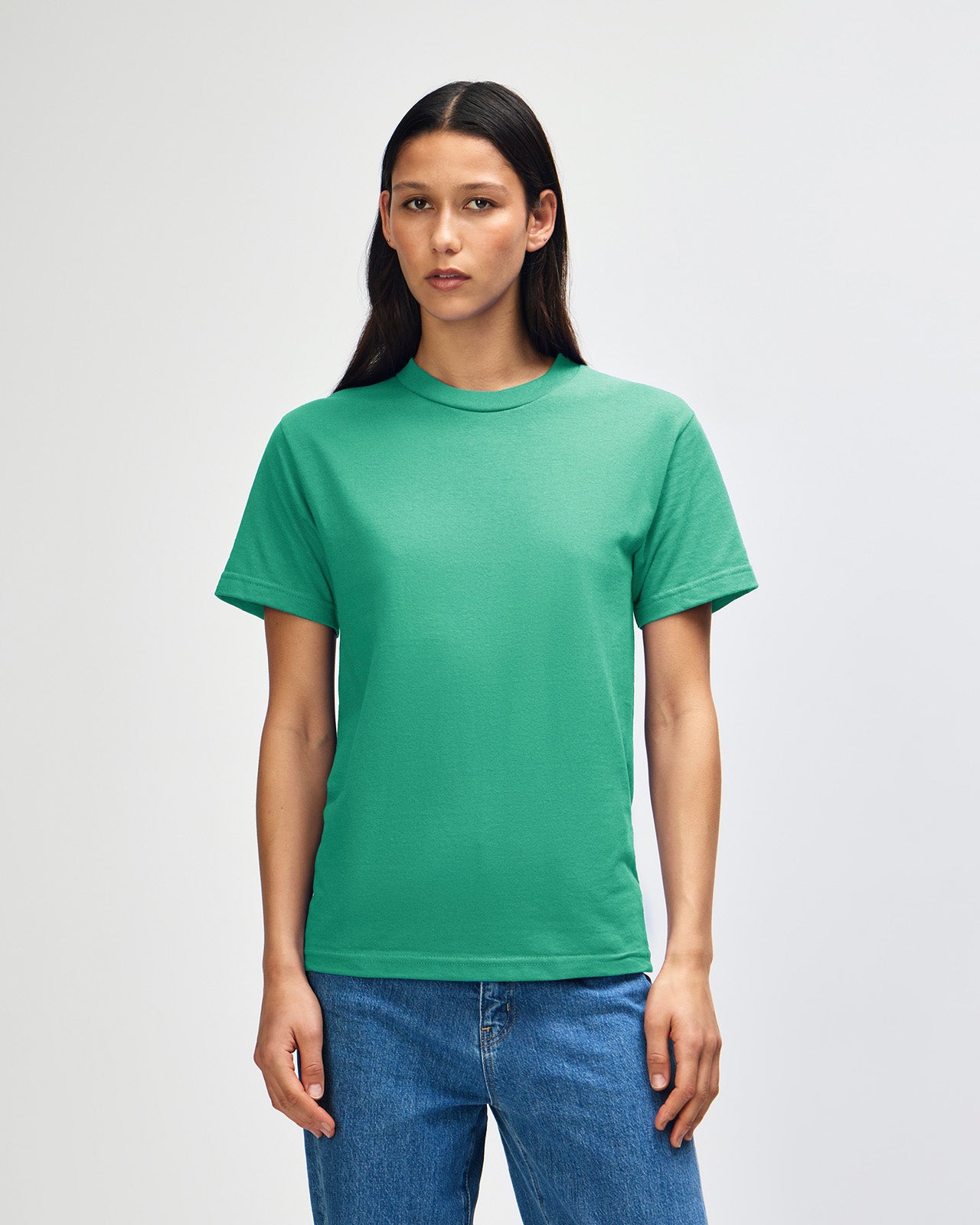 Female Model wearing a Cardinal Heavyweight Unisex Short Sleeve Crew Neck Tee, paired with blue jeans, standing against a plain background (back pose) -celadon 
