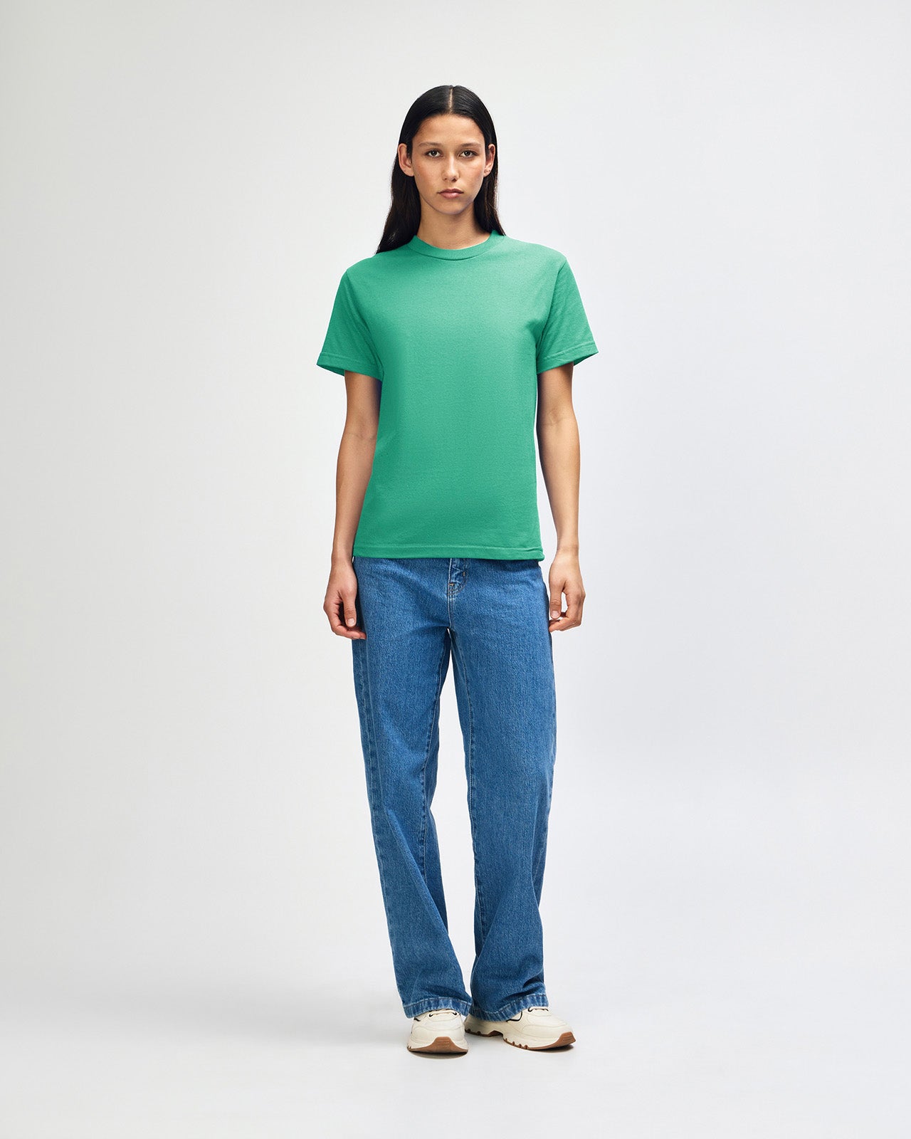 Female Model wearing a Cardinal Heavyweight Unisex Short Sleeve Crew Neck Tee, paired with blue jeans, standing against a plain background (back pose) -celadon 