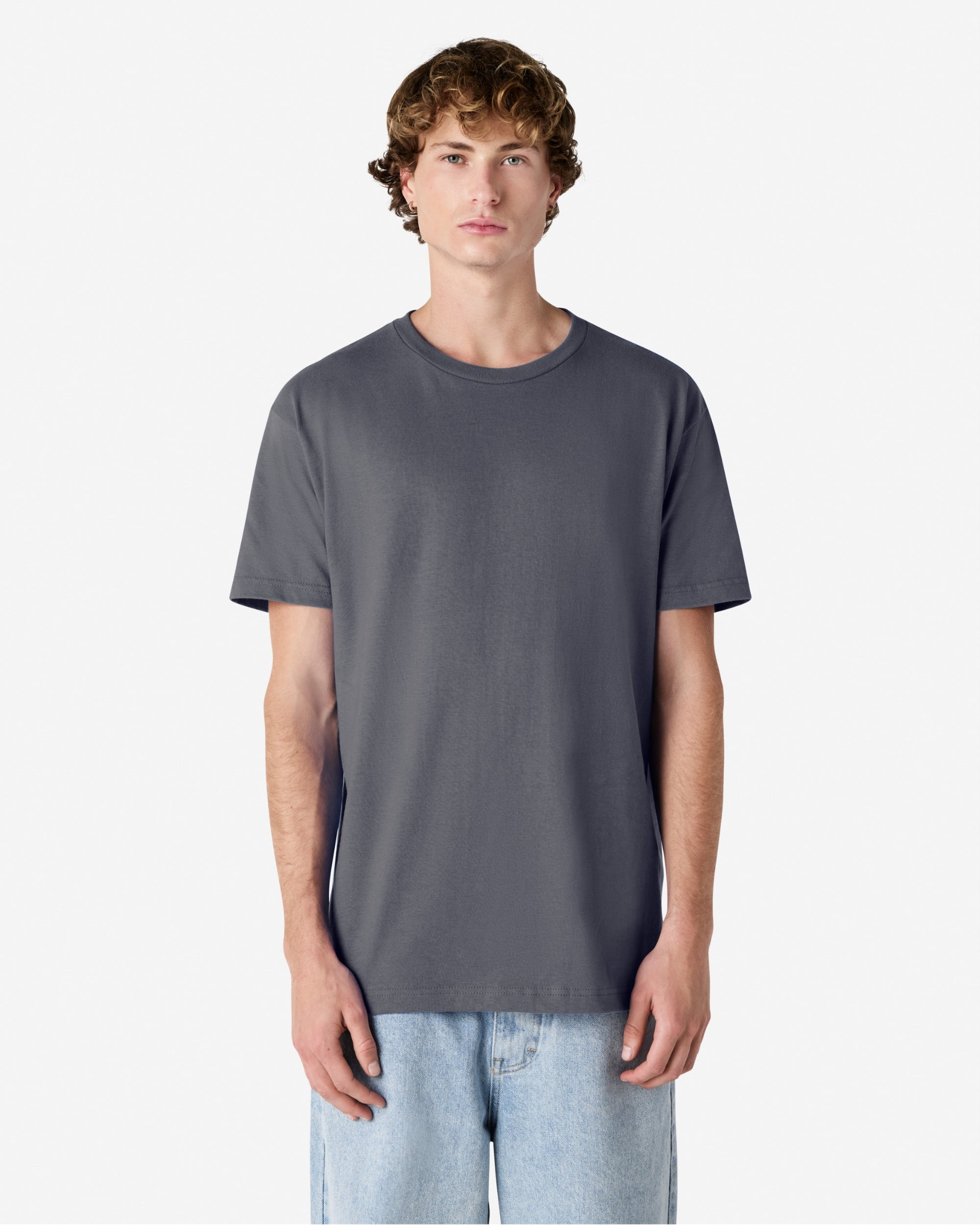 Male Model wearing a Charcoal Heavyweight Unisex Short Sleeve Crew Neck Tee, paired with blue jeans, standing against a plain background (front pose) -charcoal