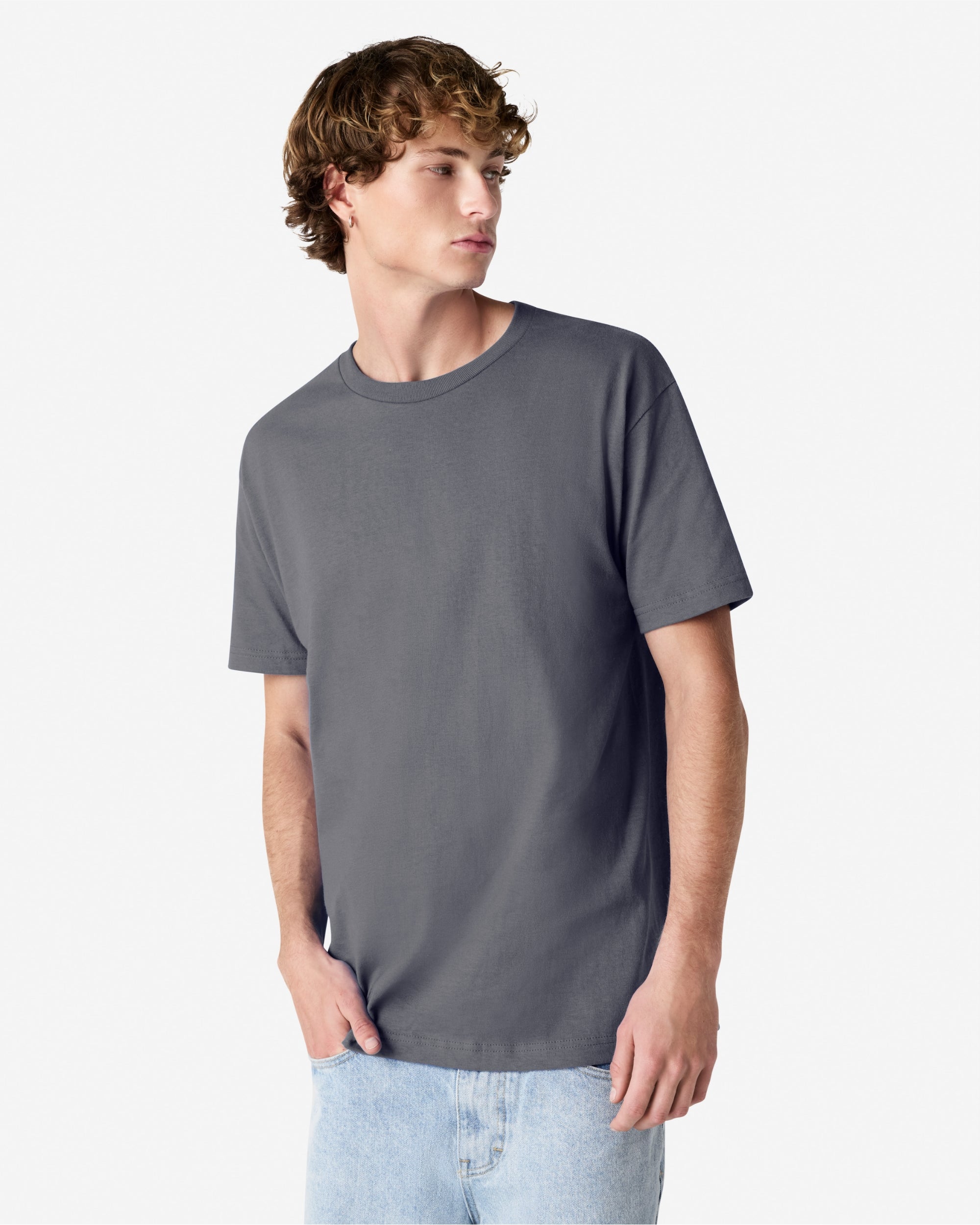 Male Model wearing a Charcoal Heavyweight Unisex Short Sleeve Crew Neck Tee, paired with blue jeans, standing against a plain background (front pose) -charcoal