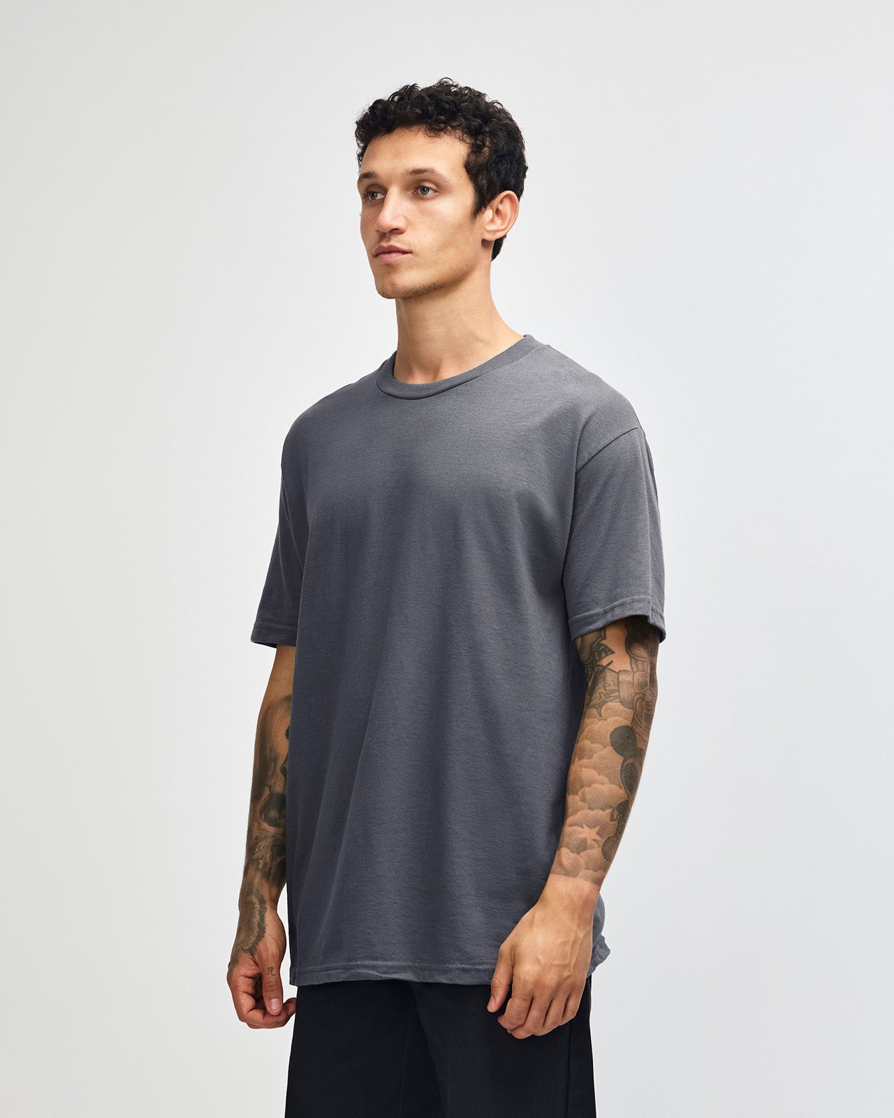 Male Model wearing a Charcoal Heavyweight Unisex Short Sleeve Crew Neck Tee, paired with blue jeans, standing against a plain background (front pose) -charcoal